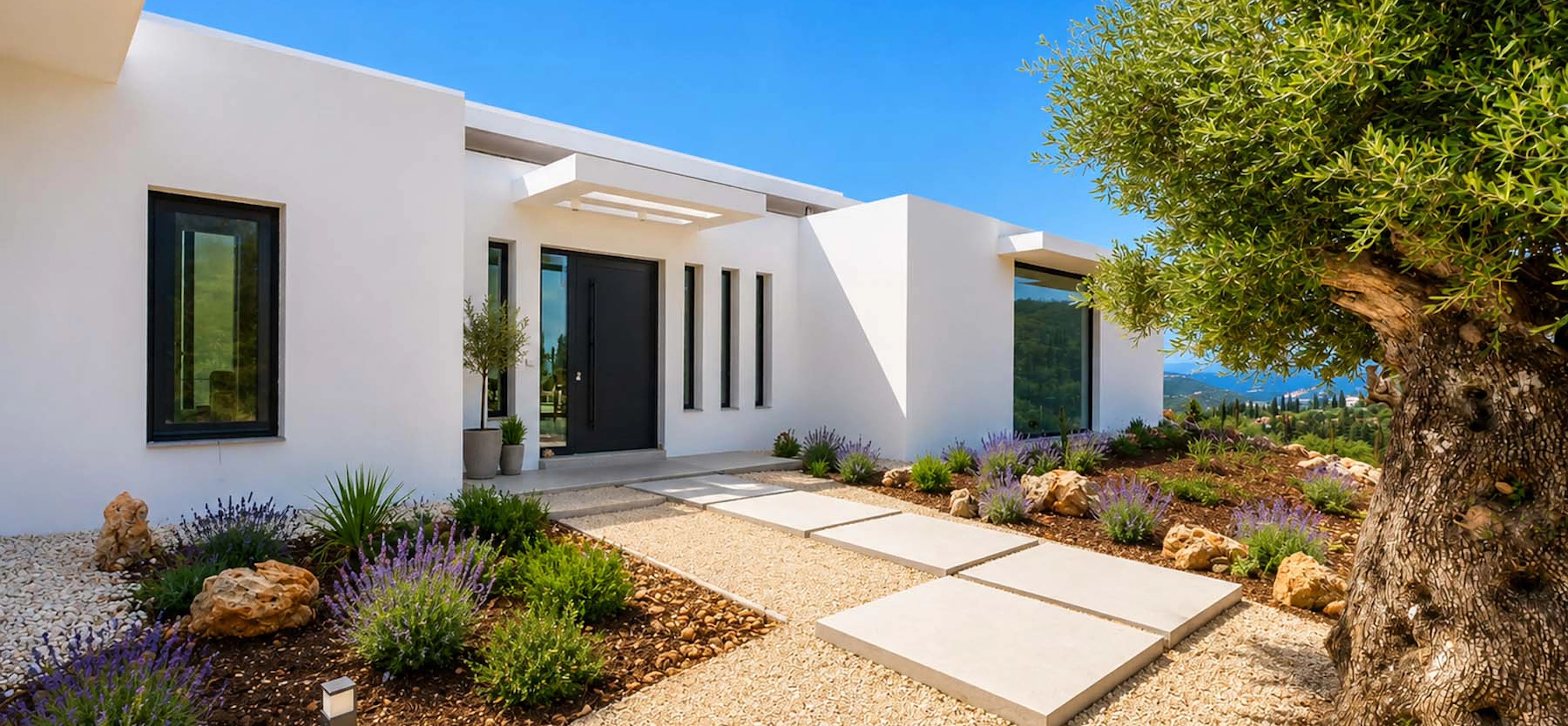 Villa entrance facade with a black front door, clean white render, stepping-stone pathway through lavender, rosemary and rock plantings, and a mature olive tree to the right