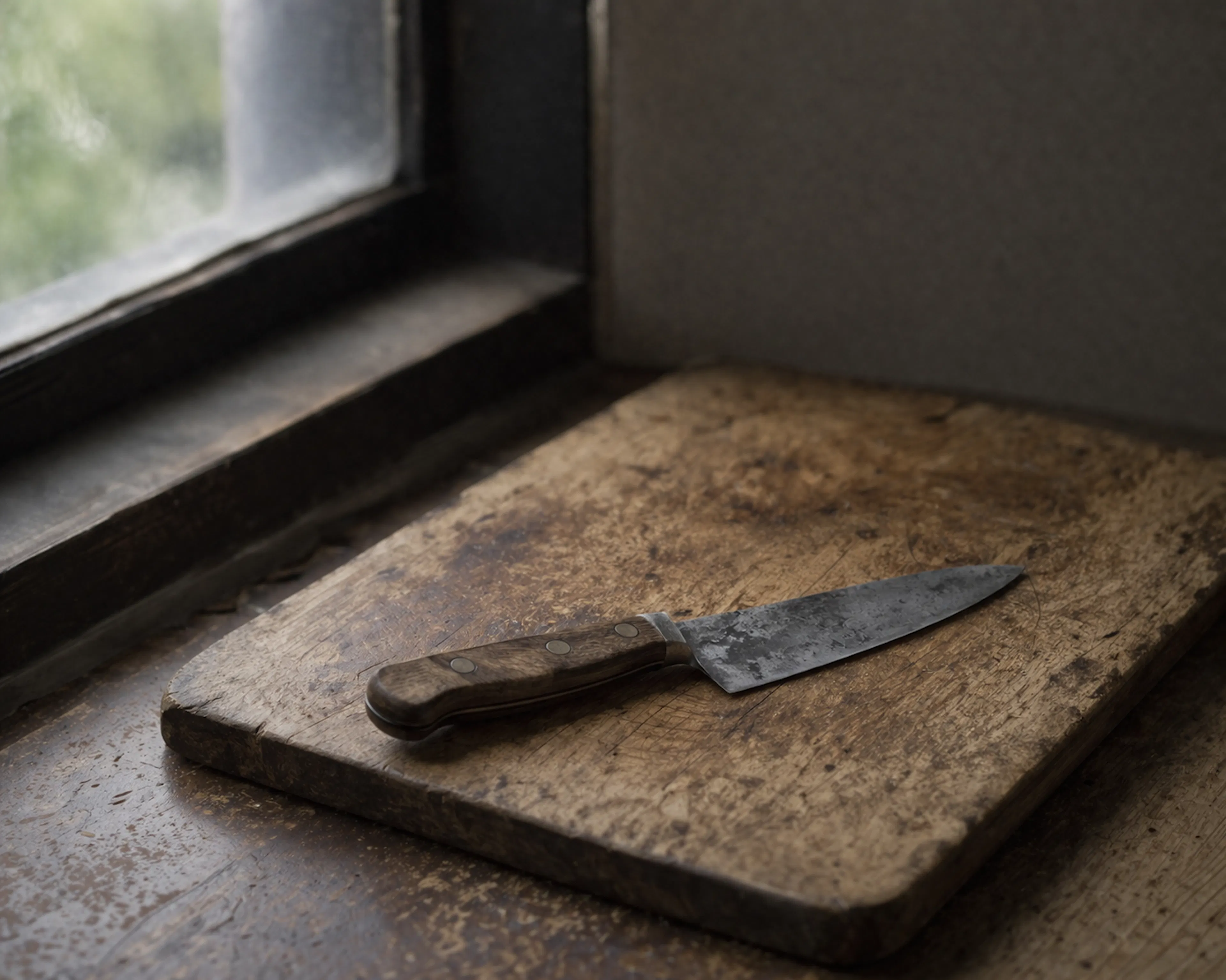 A single well-used chef's knife lying on a worn wooden chopping board