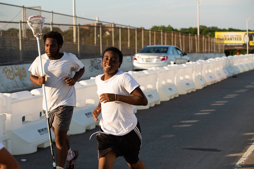 Members of a local lacrosse team run across the path, protected by water-filled barriers.