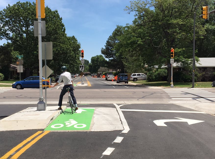 A bicyclists waits at an intersection, taking advantage of the protected bike lane.