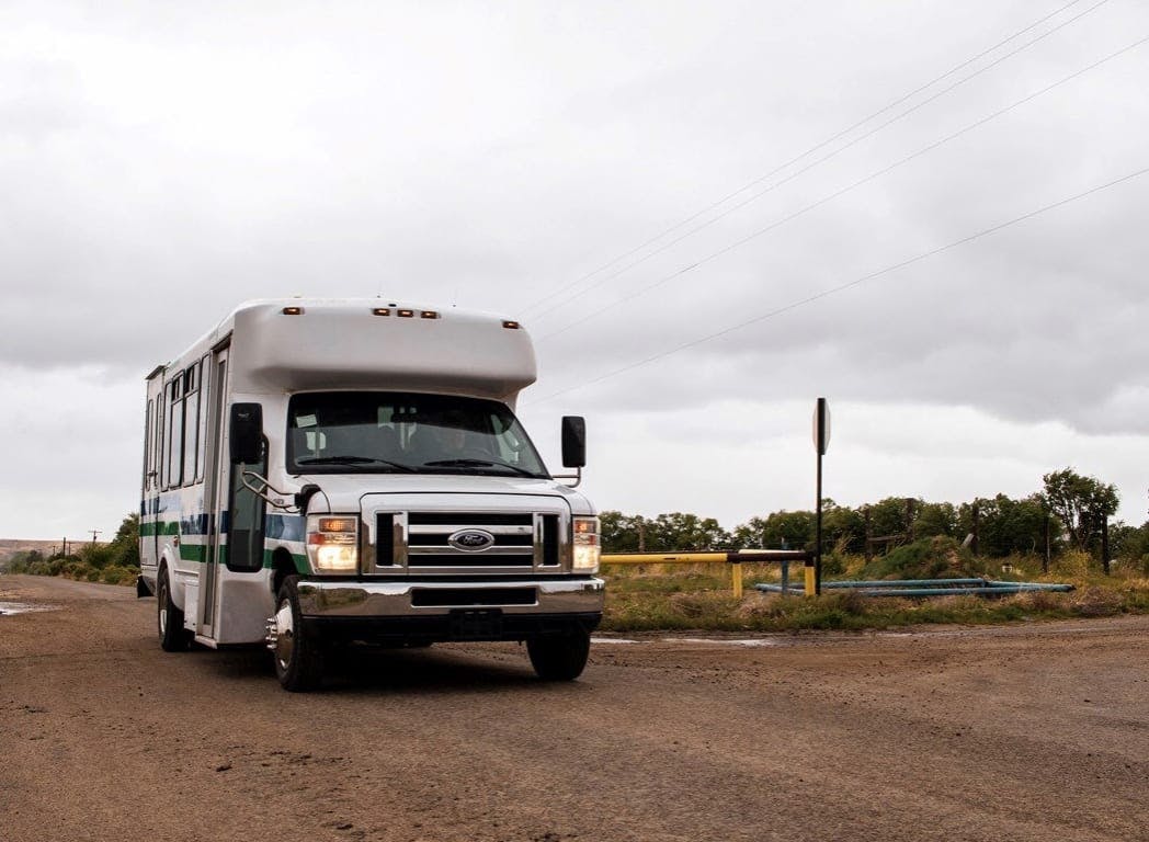 A cutaway transit bus traveling on a tribal gravel rural road near Farmington, New Mexico. (Credit: Capacity Builders)