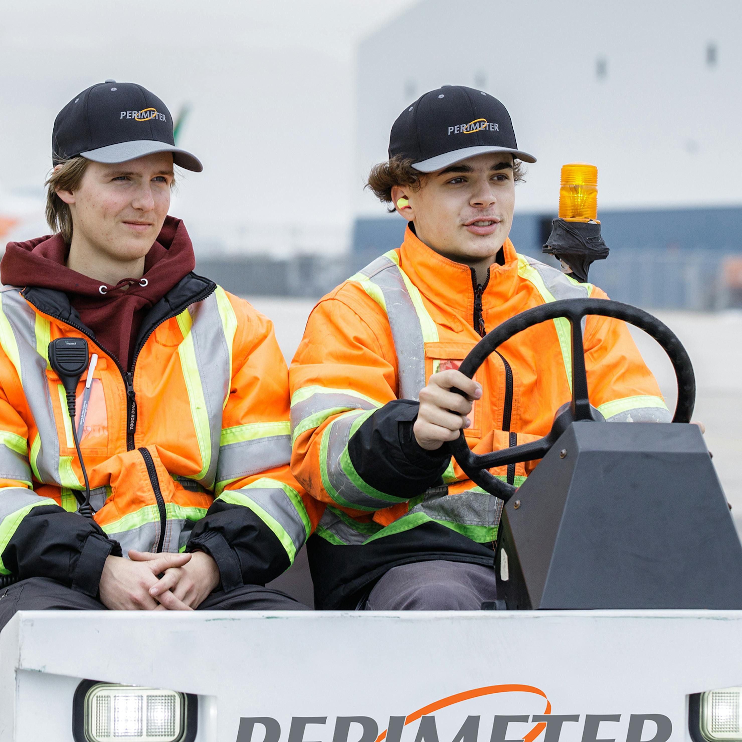 Two men on Perimeter Aviation ramp vehicle, one is driving.