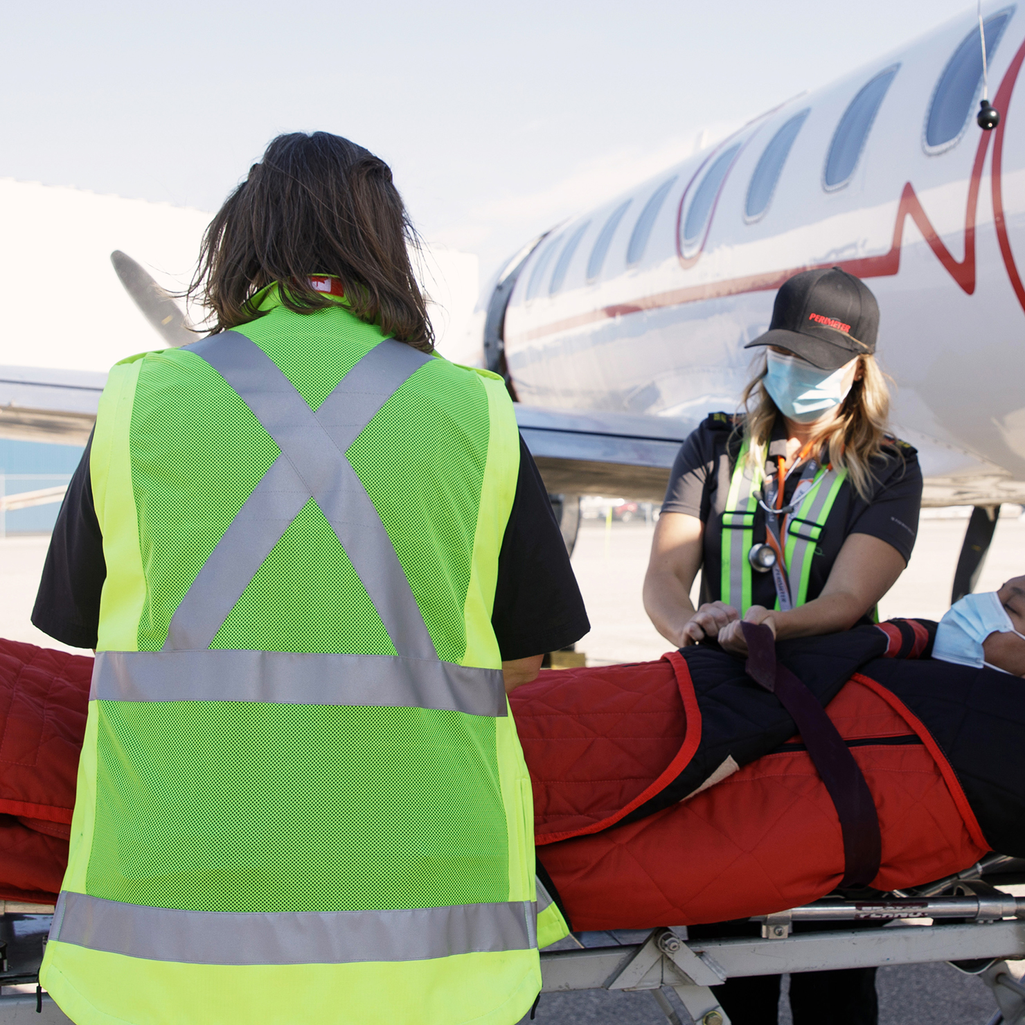 Two women medevac personnel securing patient to airplane lift.