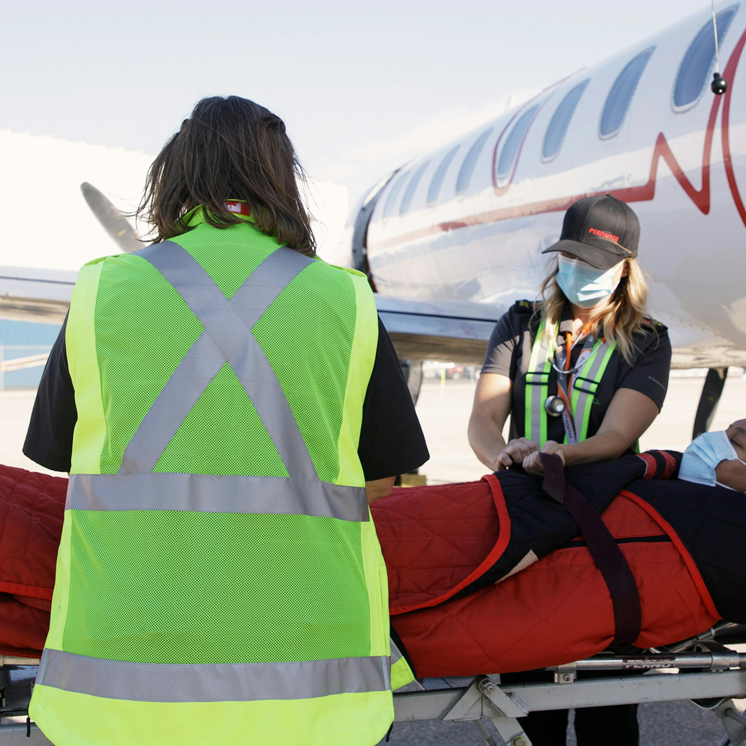 Two women medevac personnel securing patient to airplane lift.