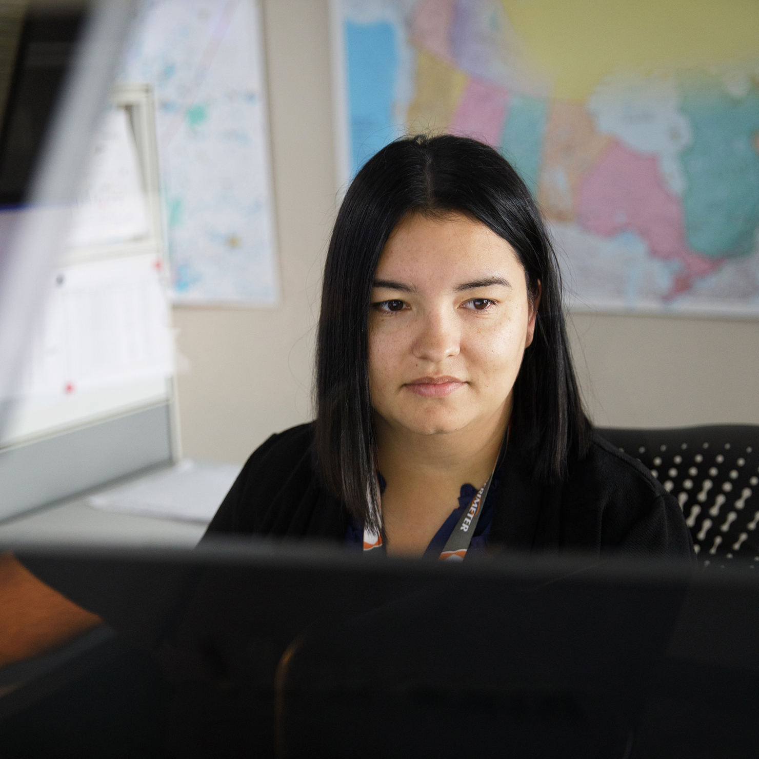 Woman looking at computer screens with map behind her on the wall.