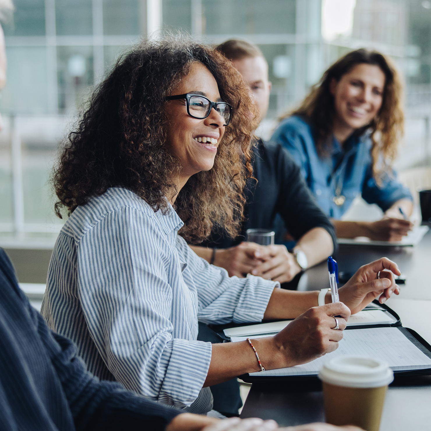 Woman smiling at someone speaking in a boardroom with two other people in the background.