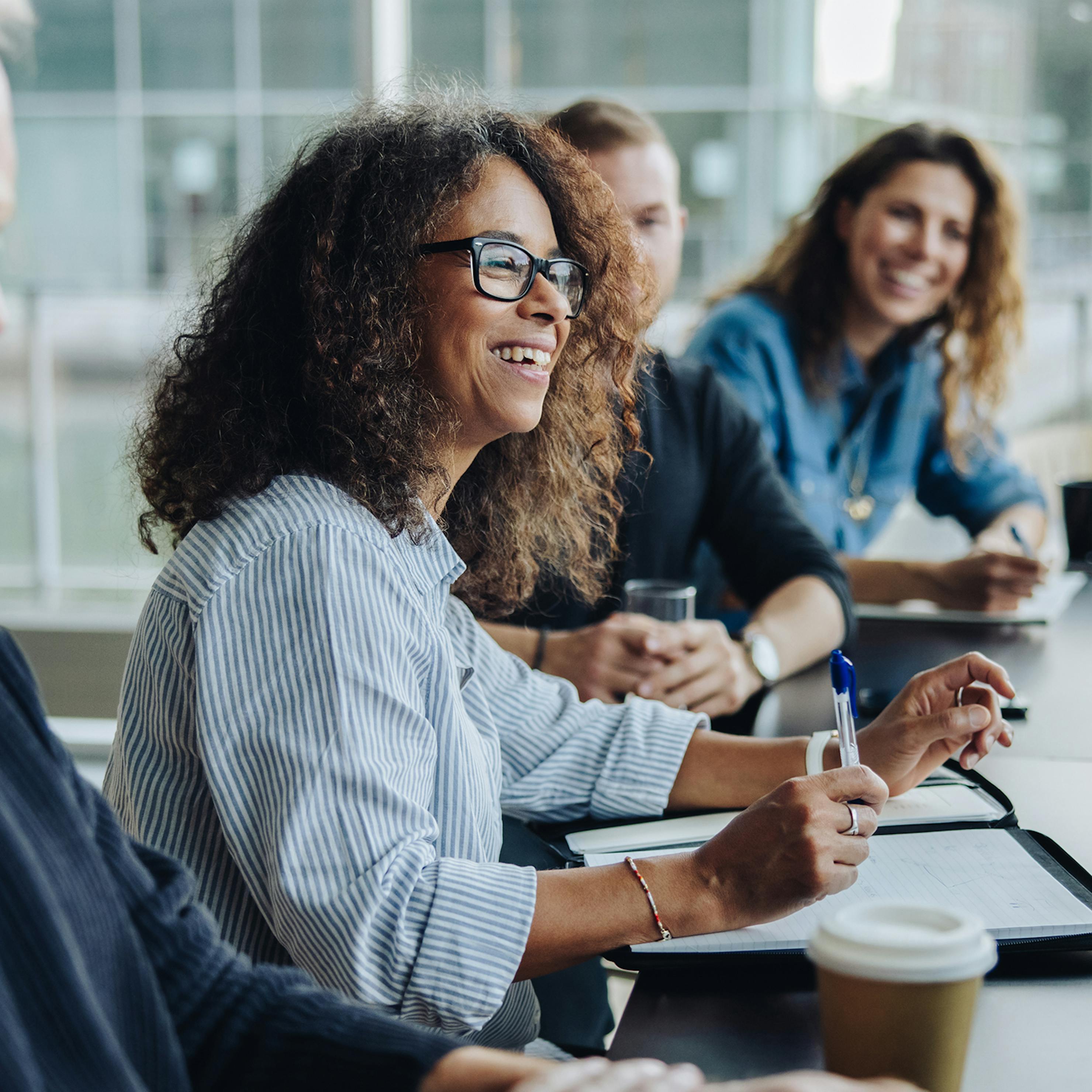 Woman smiling at someone speaking in a boardroom with two other people in the background.