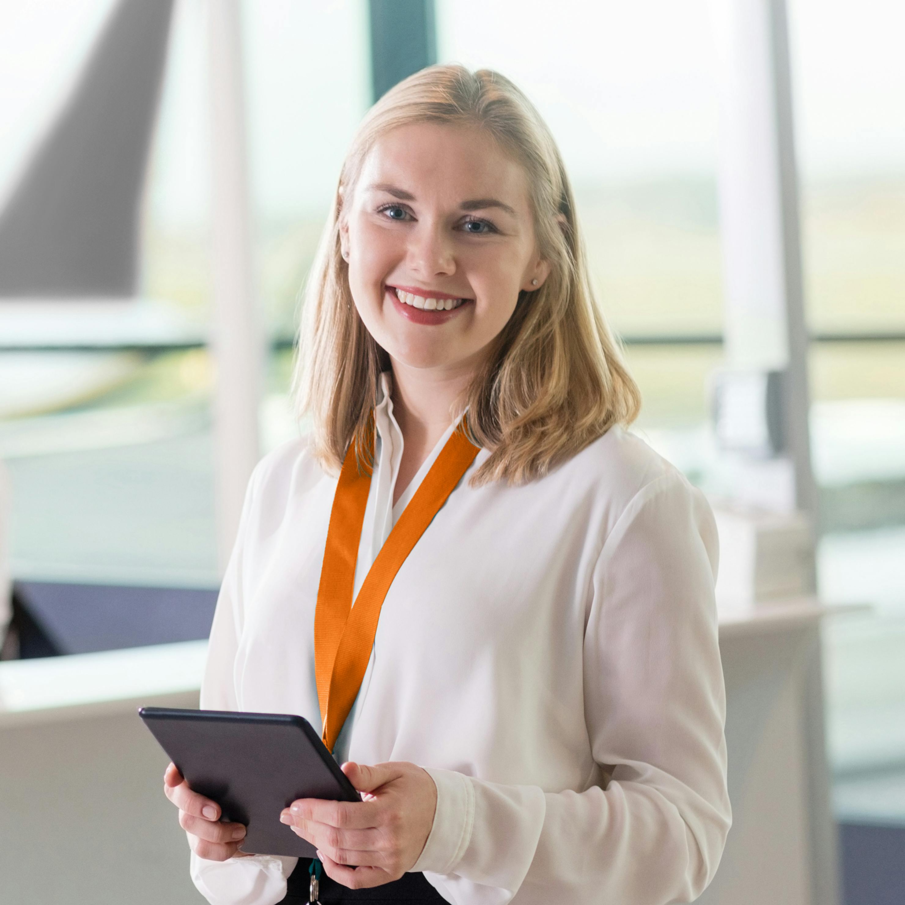 Woman holding tablet in a boarding lounge and smiling at camera.