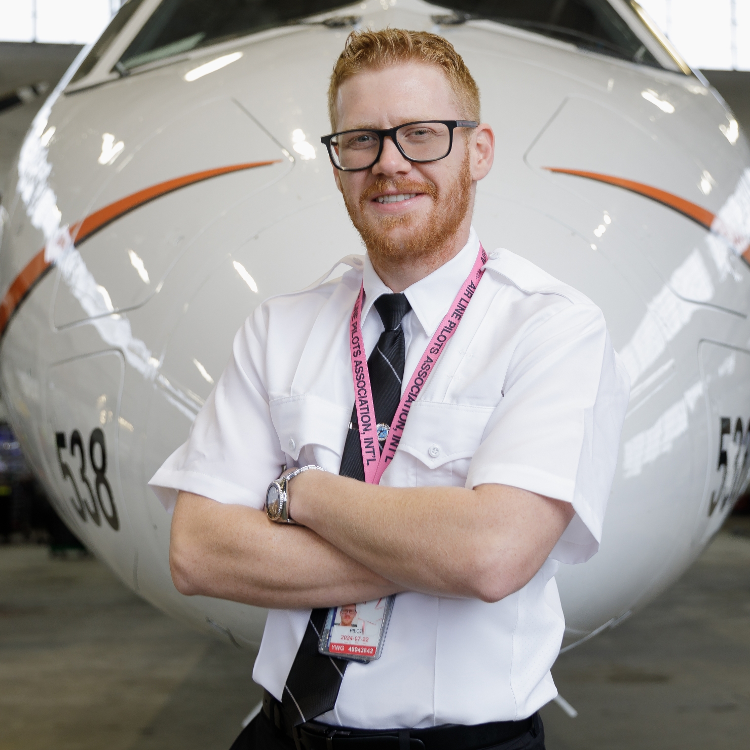 Male pilot standing with arms crossed in front of an airplane.