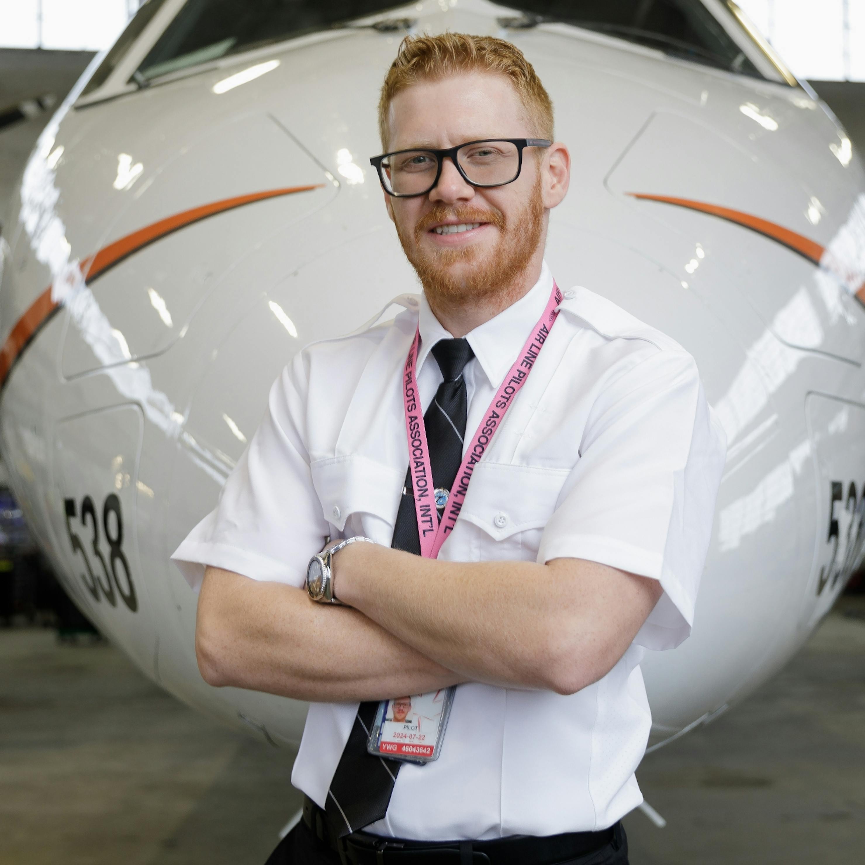 Male pilot standing with arms crossed in front of an airplane.