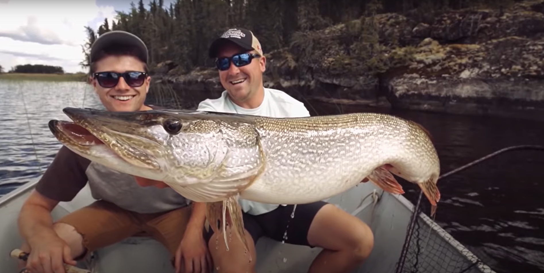 Father and son holding a fish, sitting in a boat on a lake.