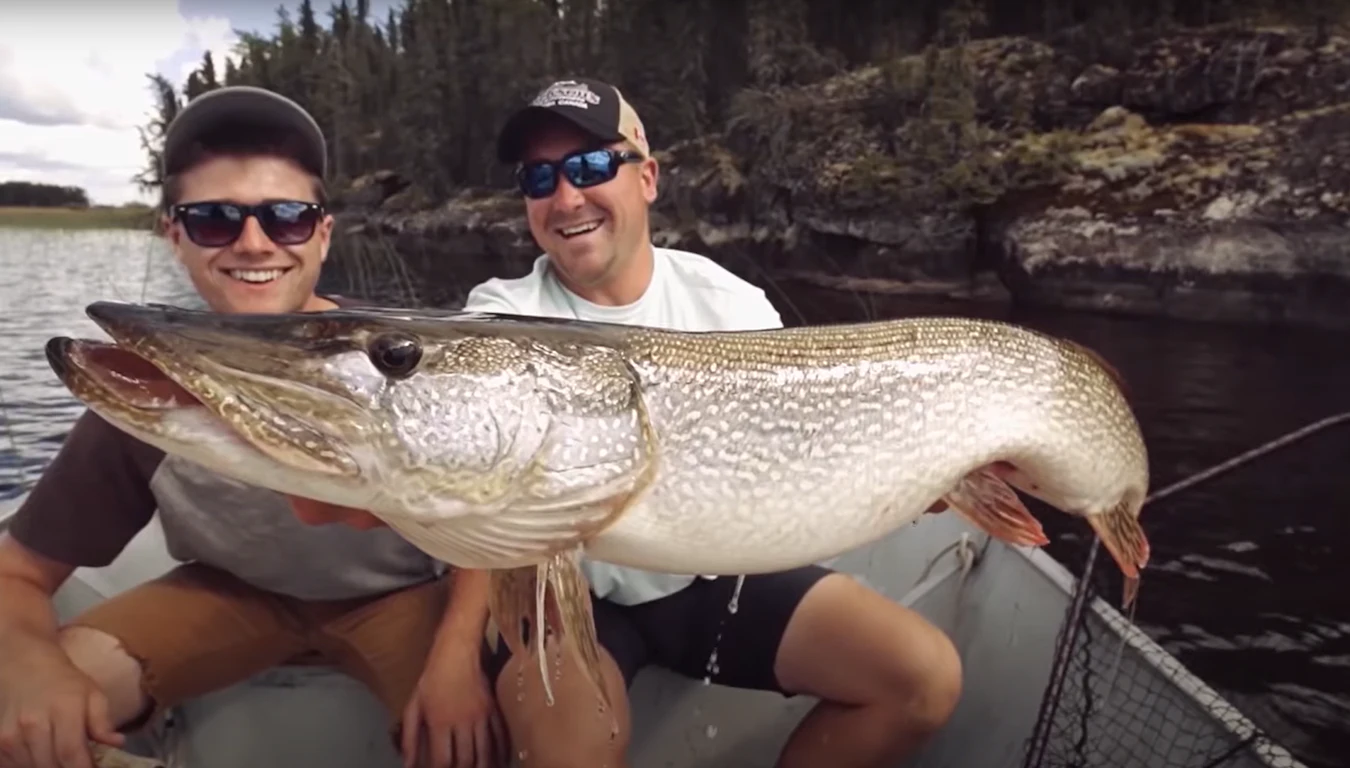 Father and son holding a fish, sitting in a boat on a lake.