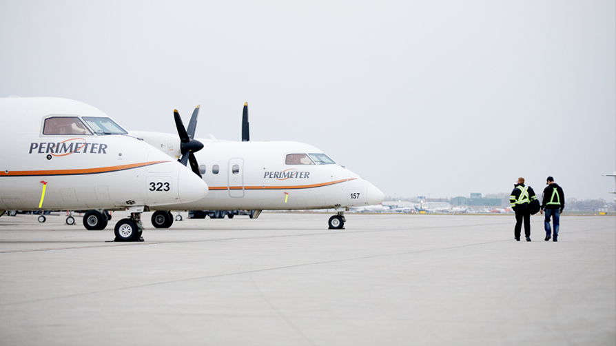 Two men walking towards two Perimeter Aviation airplanes.