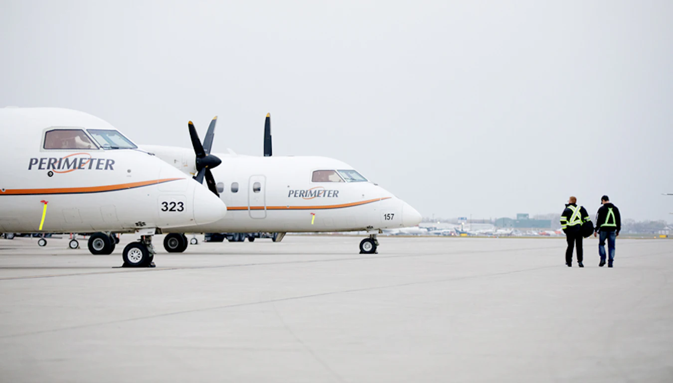 Two men walking towards two Perimeter Aviation airplanes.