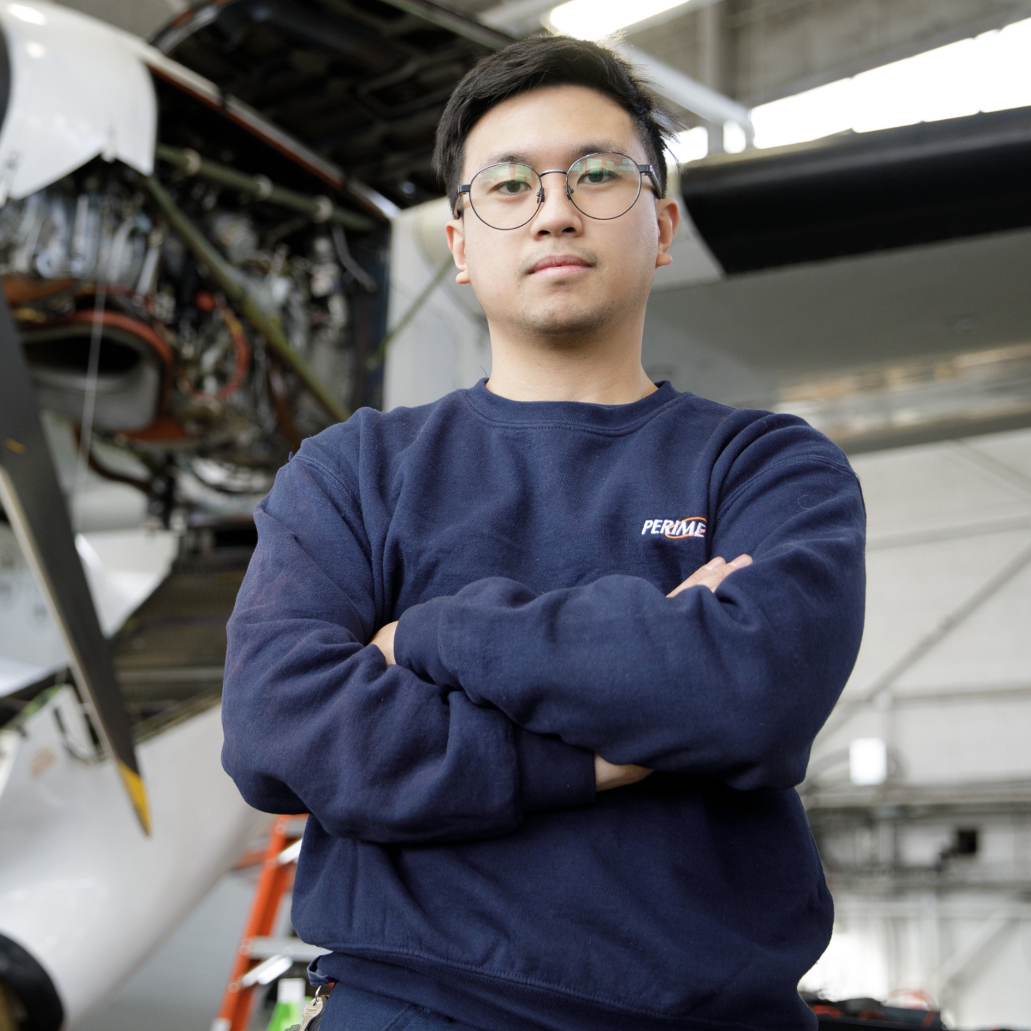 Male avionics AME standing with arms crossed in a hangar.