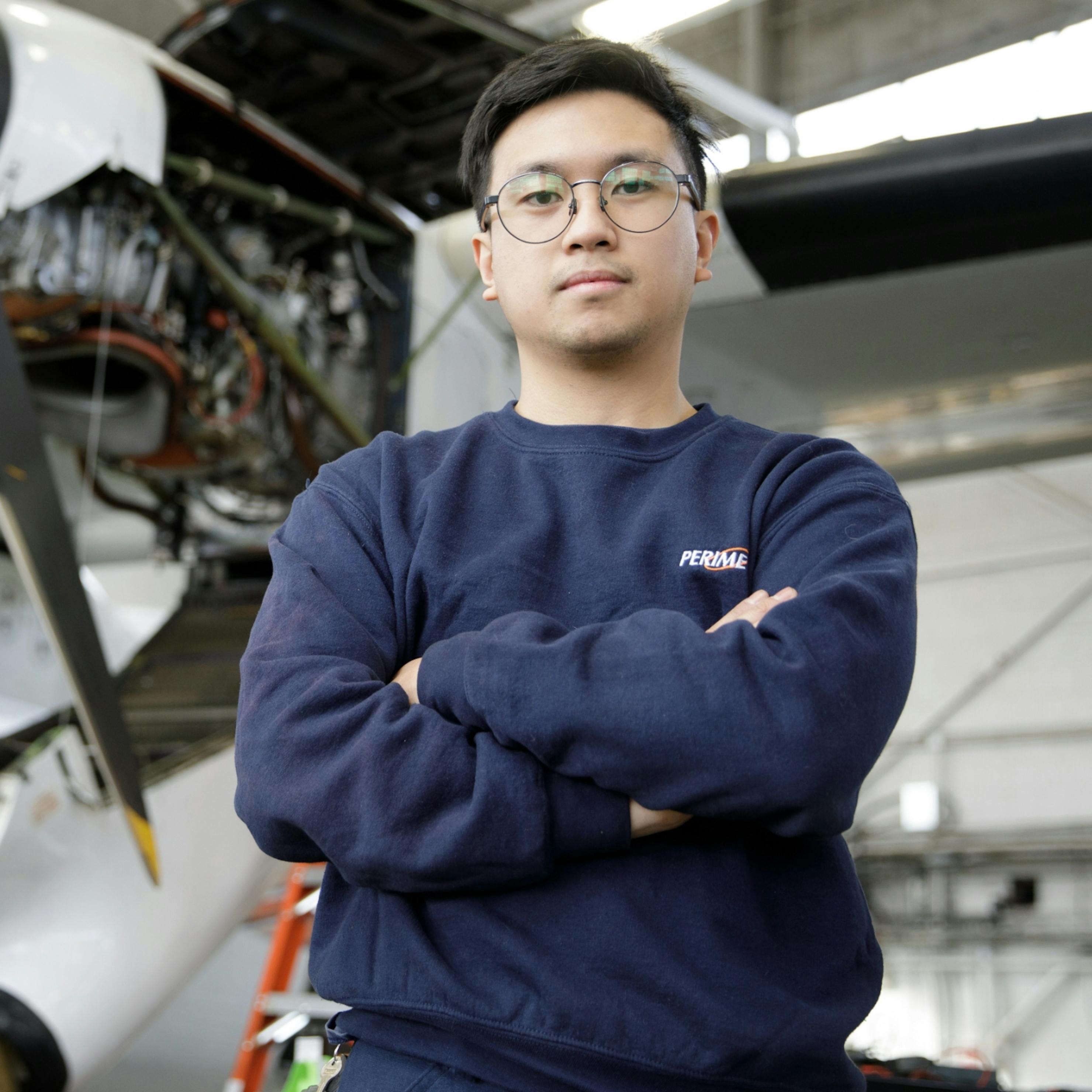 Male avionics AME standing with arms crossed in a hangar.