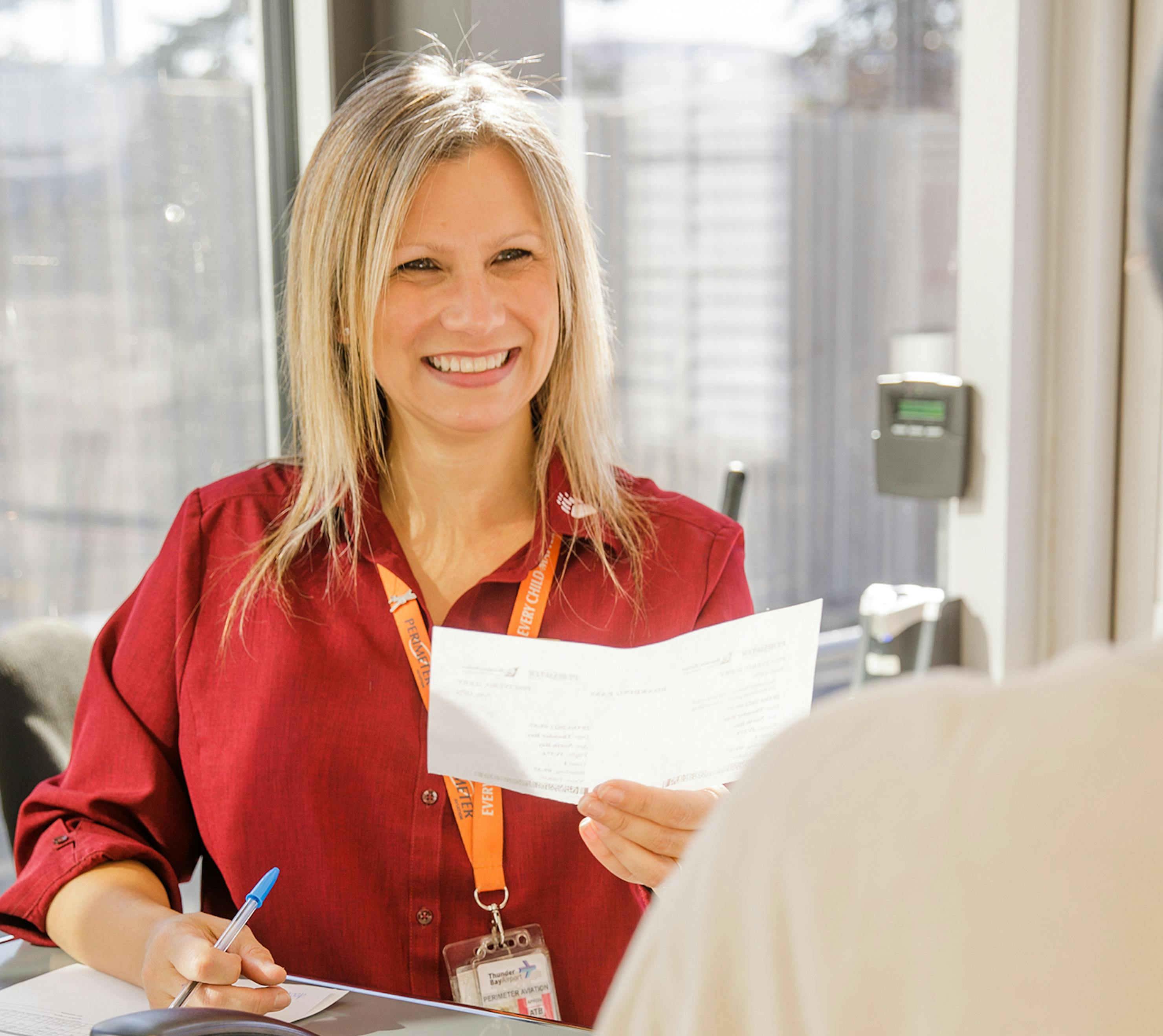 Woman holding boarding pass and pen and smiling at passenger.