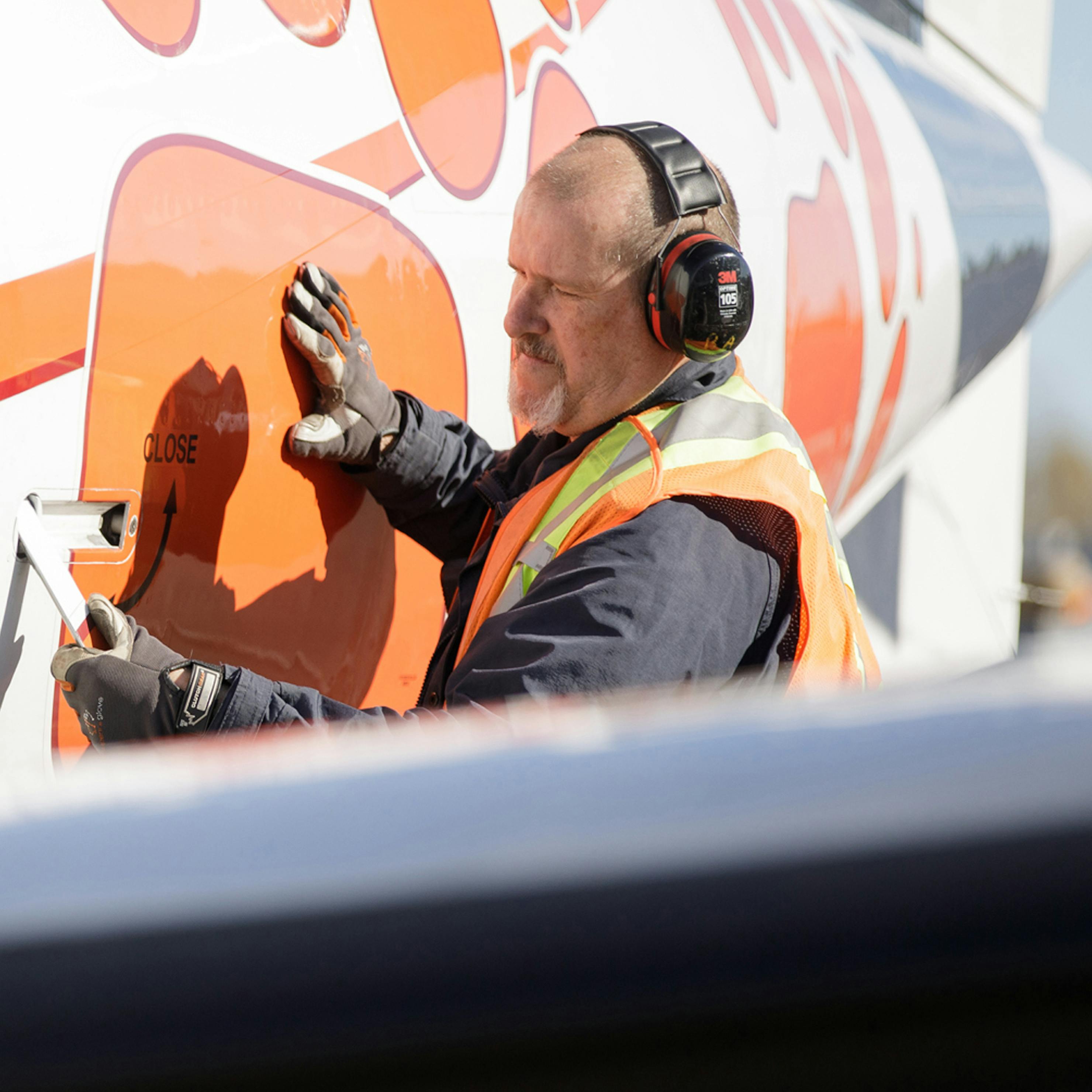 Man closing the cargo door on an aircraft while wearing hearing protection.