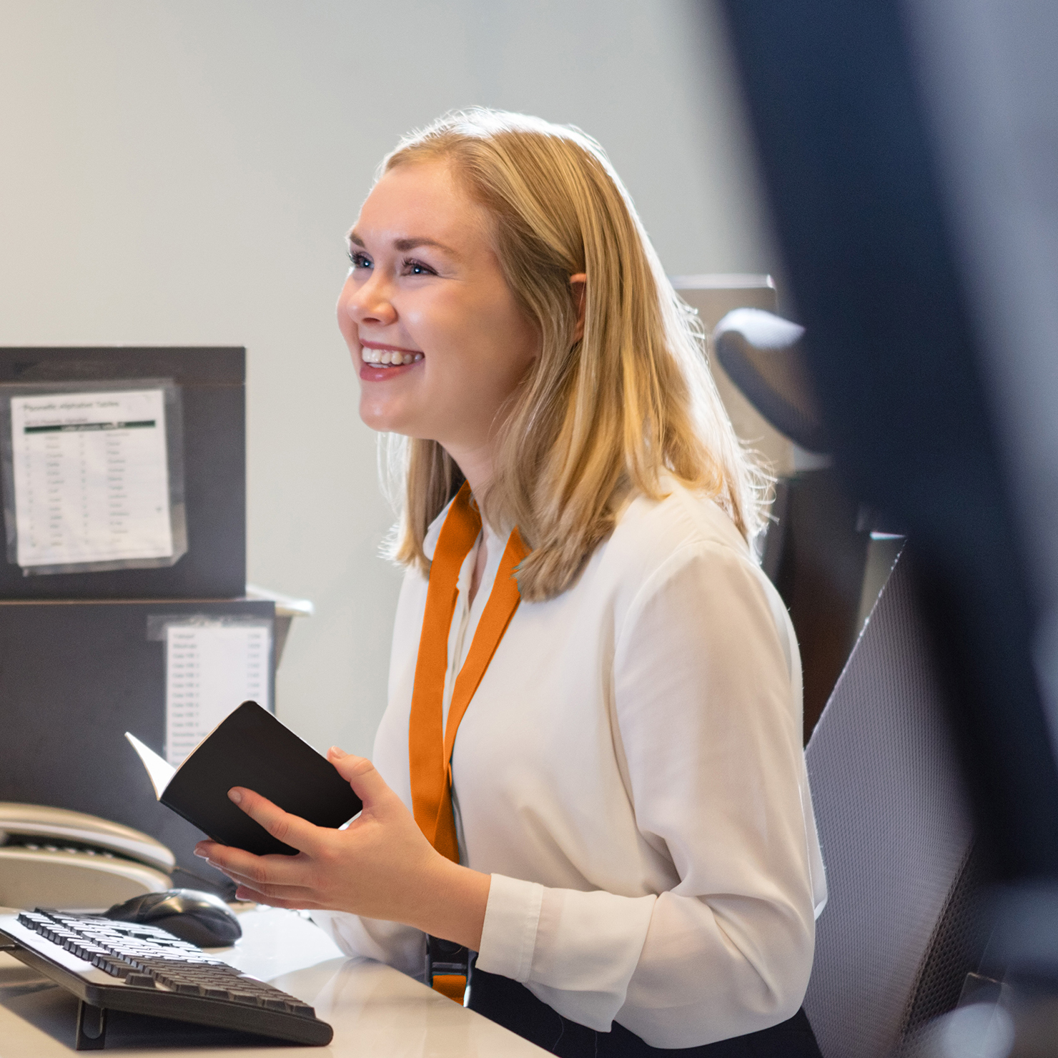 Woman at the check-in counter looking at a ID document and smiling off camera to a passenger.
