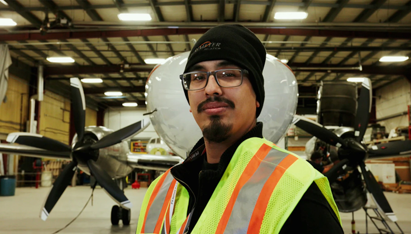 Man wearing a reflective vest standing in front of an airplane in a hangar.