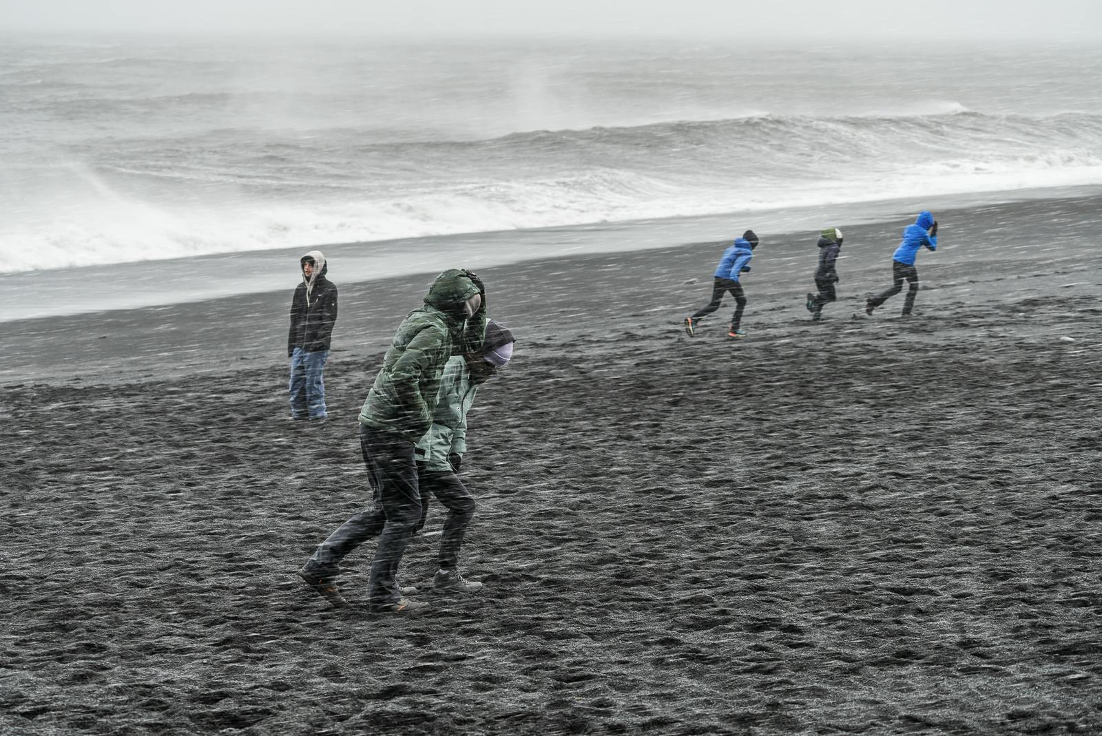 tourists in bad weather at reynisfjara iceland with waves in background
