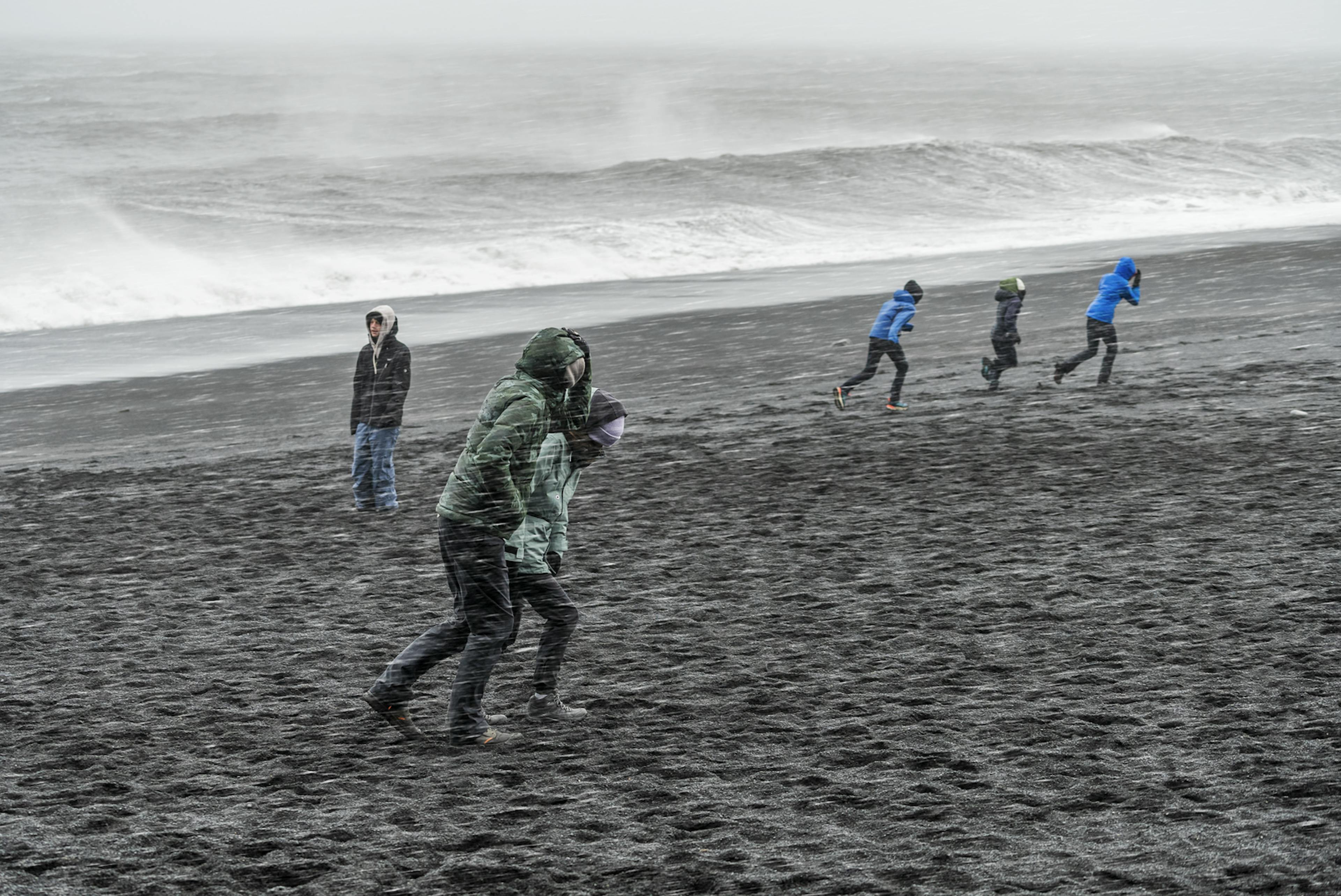 tourists in bad weather at reynisfjara iceland with waves in background