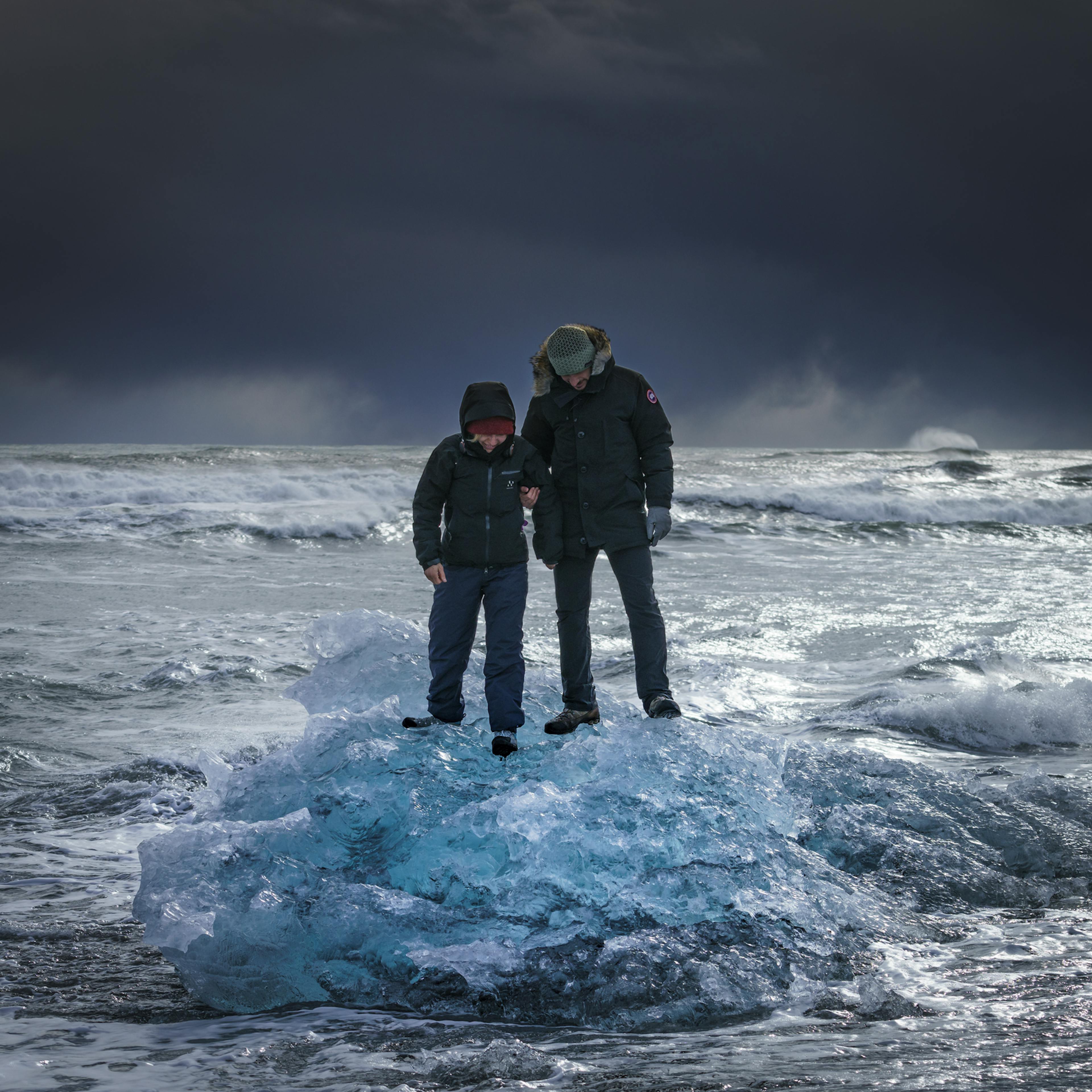 tourists standing on a small iceberg in on diamond beach