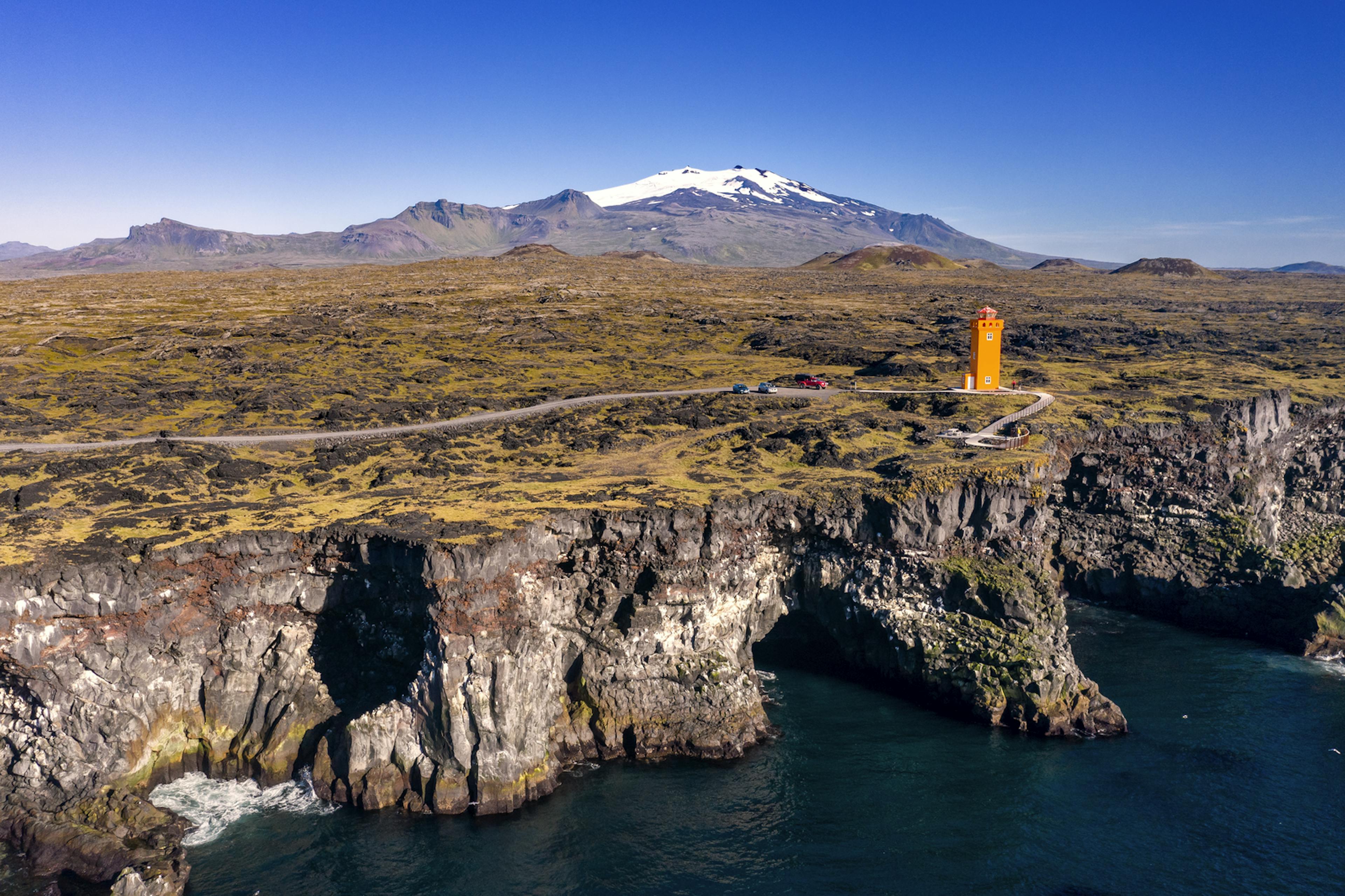 Orange lighthouse by Gerðuberg cliffs on a sunny day