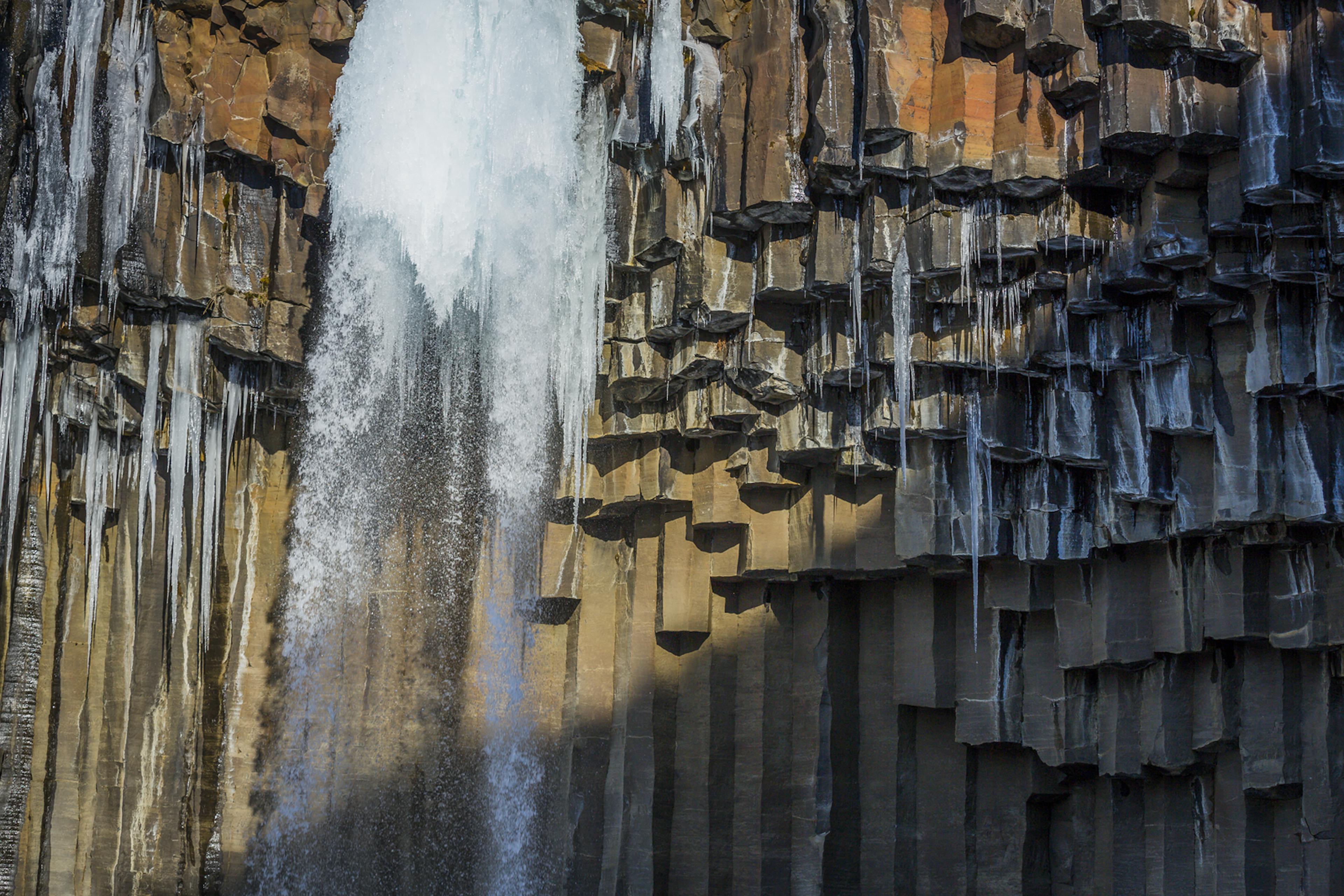 A close up of Svartifoss waterfall with frozen water and icecircles with basalt columns in the background