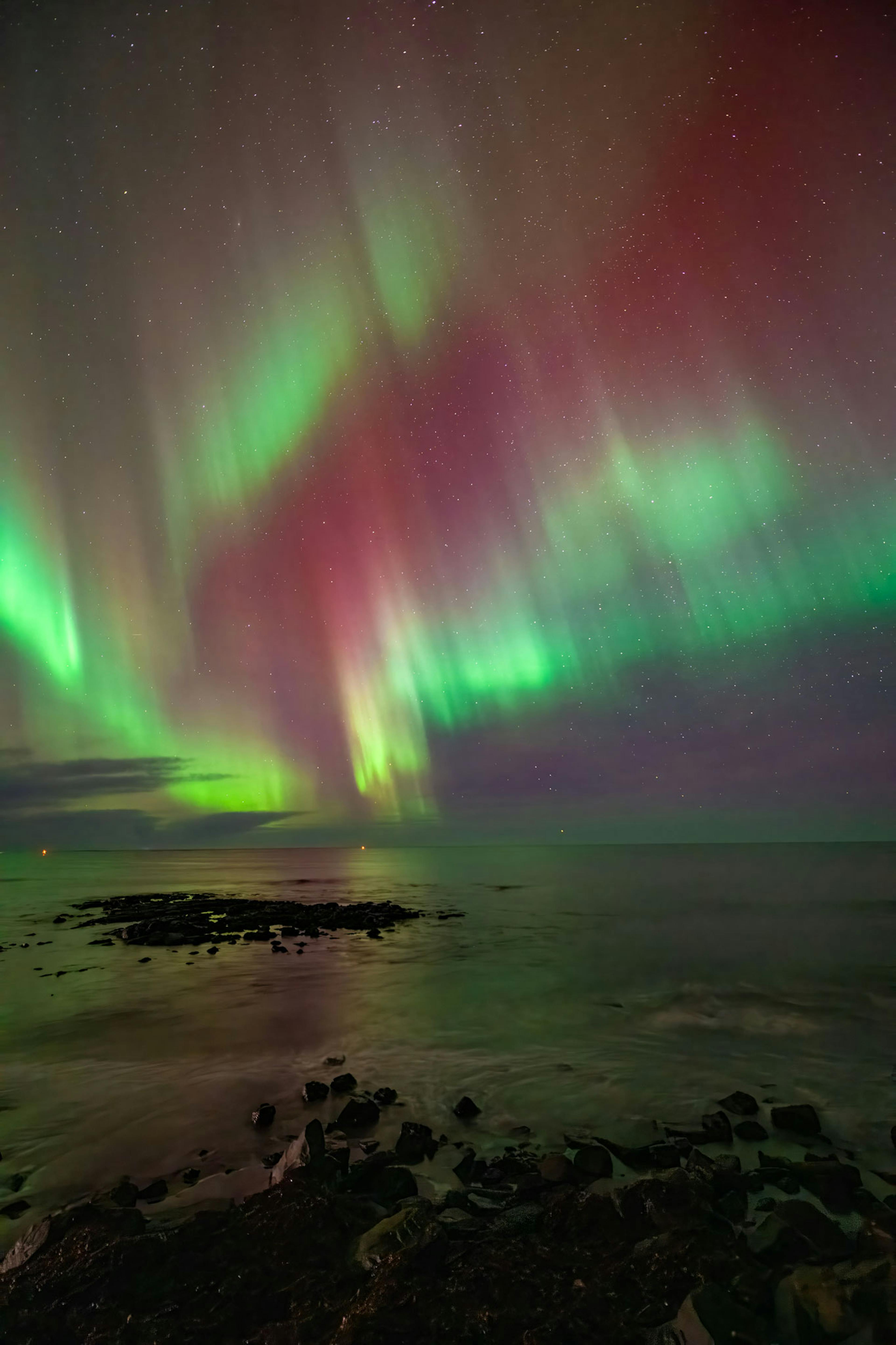 red and green northern lights over water in reykjanes