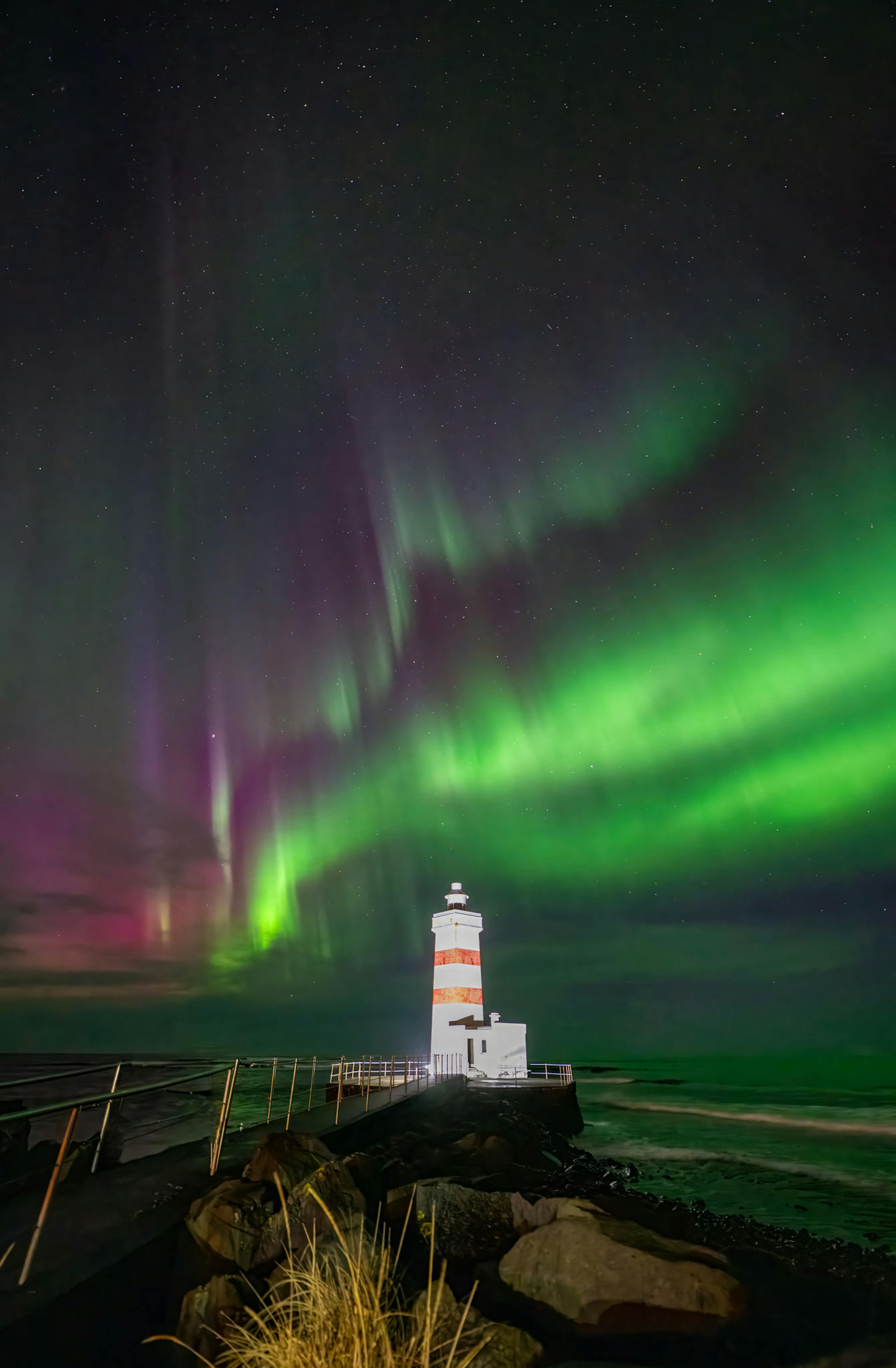 pink and green northern lights dancing over light house in iceland