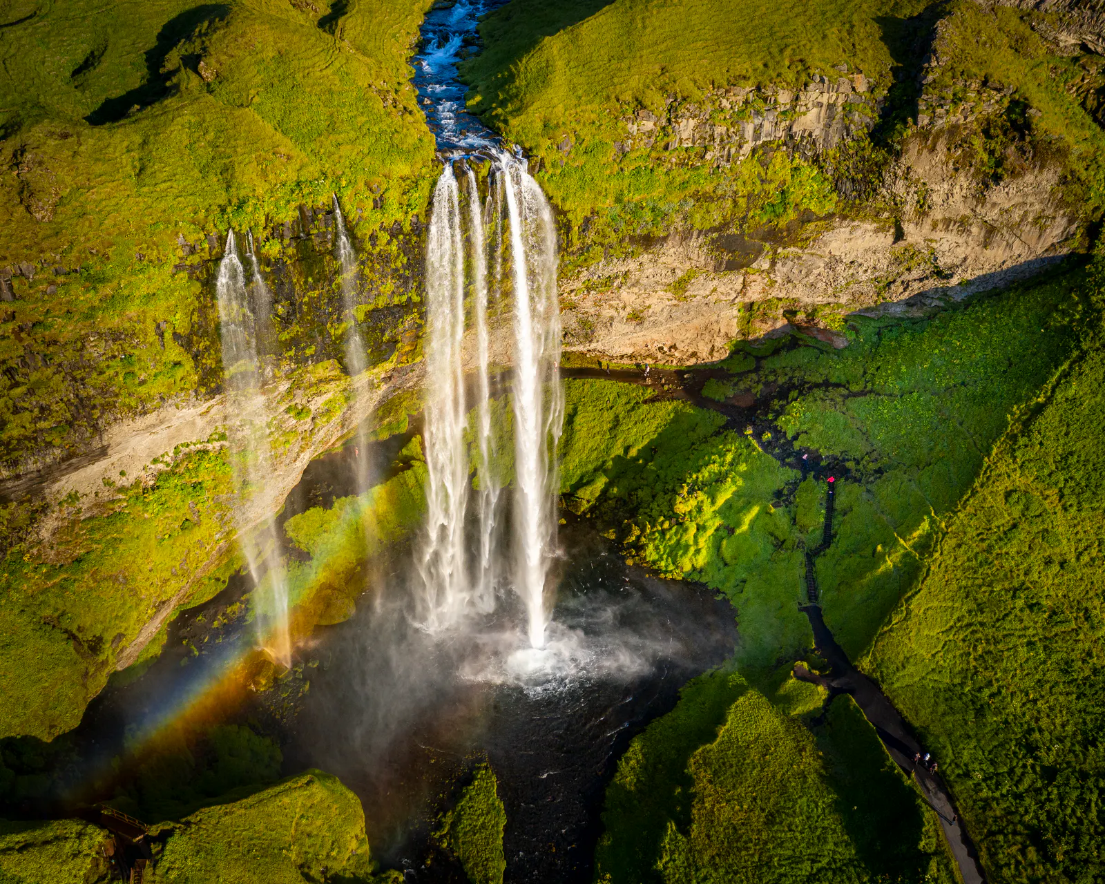 aerial view of Seljalandfoss with a faint rainbow and bright green moss