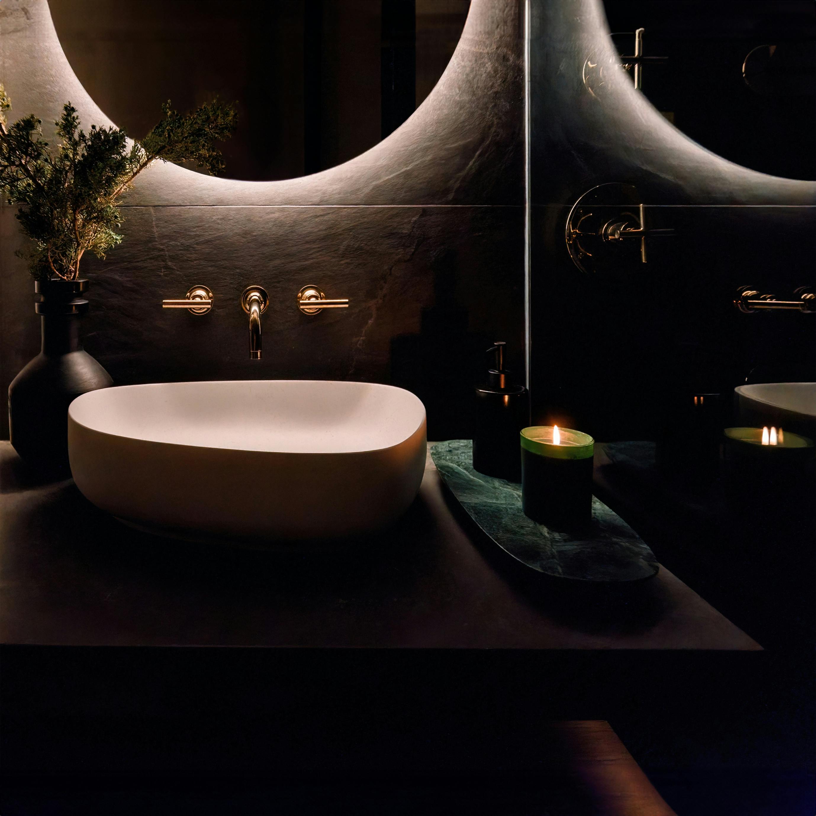 A moon-like backlit mirror casts a soft glow on the custom floating vanity that further adds to the open feeling. A pebble-shaped vessel sink and the wood tones of the storage cabinet add organic warmth – Design by Persimmon Design