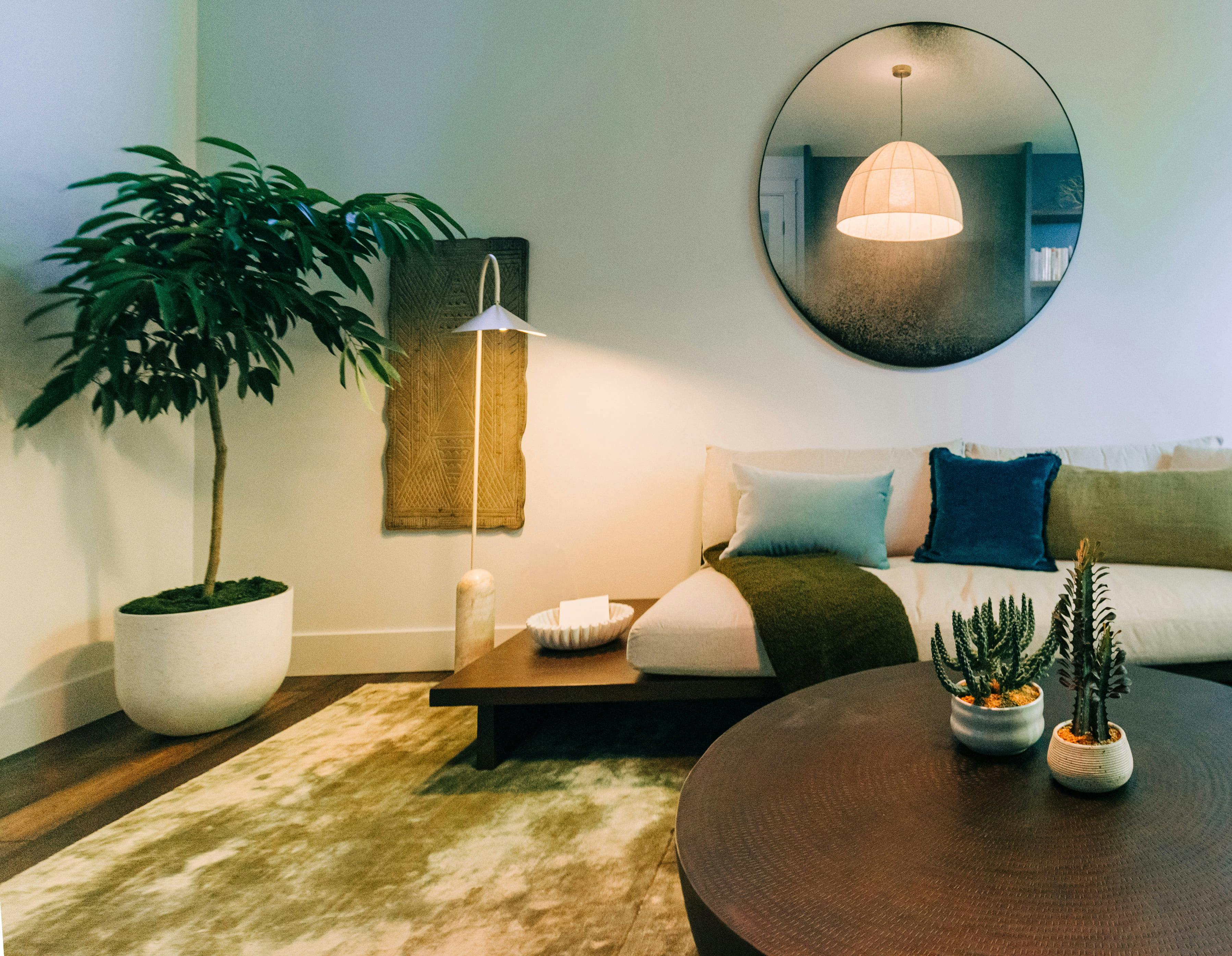 In this Wellness room by Persimmon Design, an antique mirror reflects the soft glow of a linen pendant, infusing the space with quiet character. Lush greenery and tactile layers complete the sanctuary-like setting.