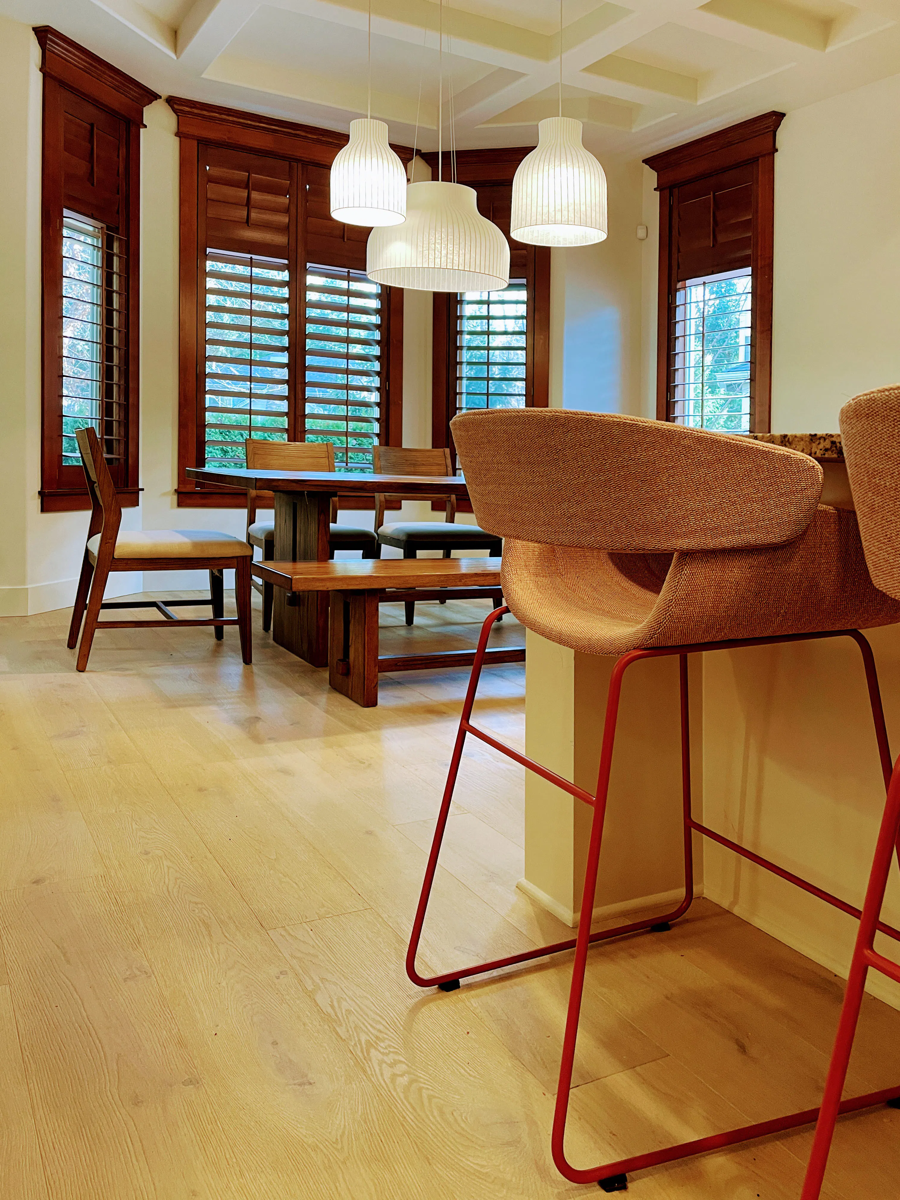 In this dining space designed by Persimmon Design, a trio of sculptural pendants animates the coffered ceiling, adding softness and rhythm while emphasizing the architectural geometry overhead.