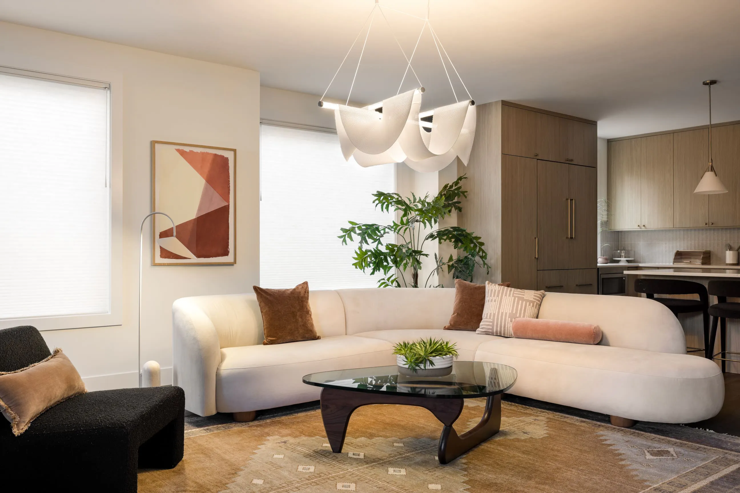 The sculptural pendant overhead in this living room room by Persimmon Design, is doing the decorative work adding personality to the space, while the arc floor lamp beside the sofa provides task light for reading, and the pendant in the kitchen beyond takes care of its own zone entirely. That's the whole idea behind layered lighting — not one fixture trying to do everything, but several working quietly together to make a space feel alive.