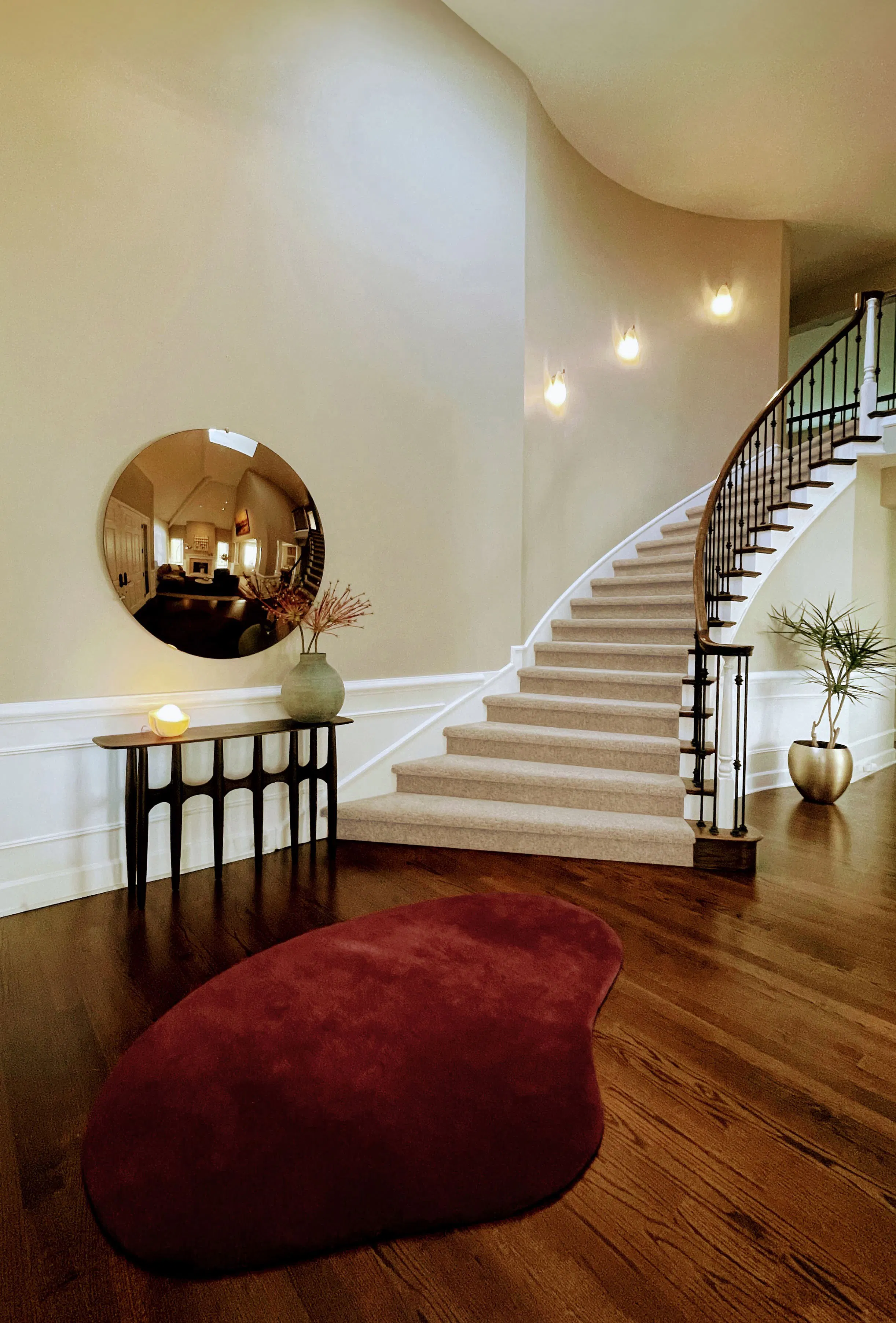 In this sweeping stairwell by Persimmon Design, high-placed sconces, and generous expanse of wall work together to turn vertical volume into something uplifting, while the low console and grounded furnishings keep the space from losing its sense of welcome.