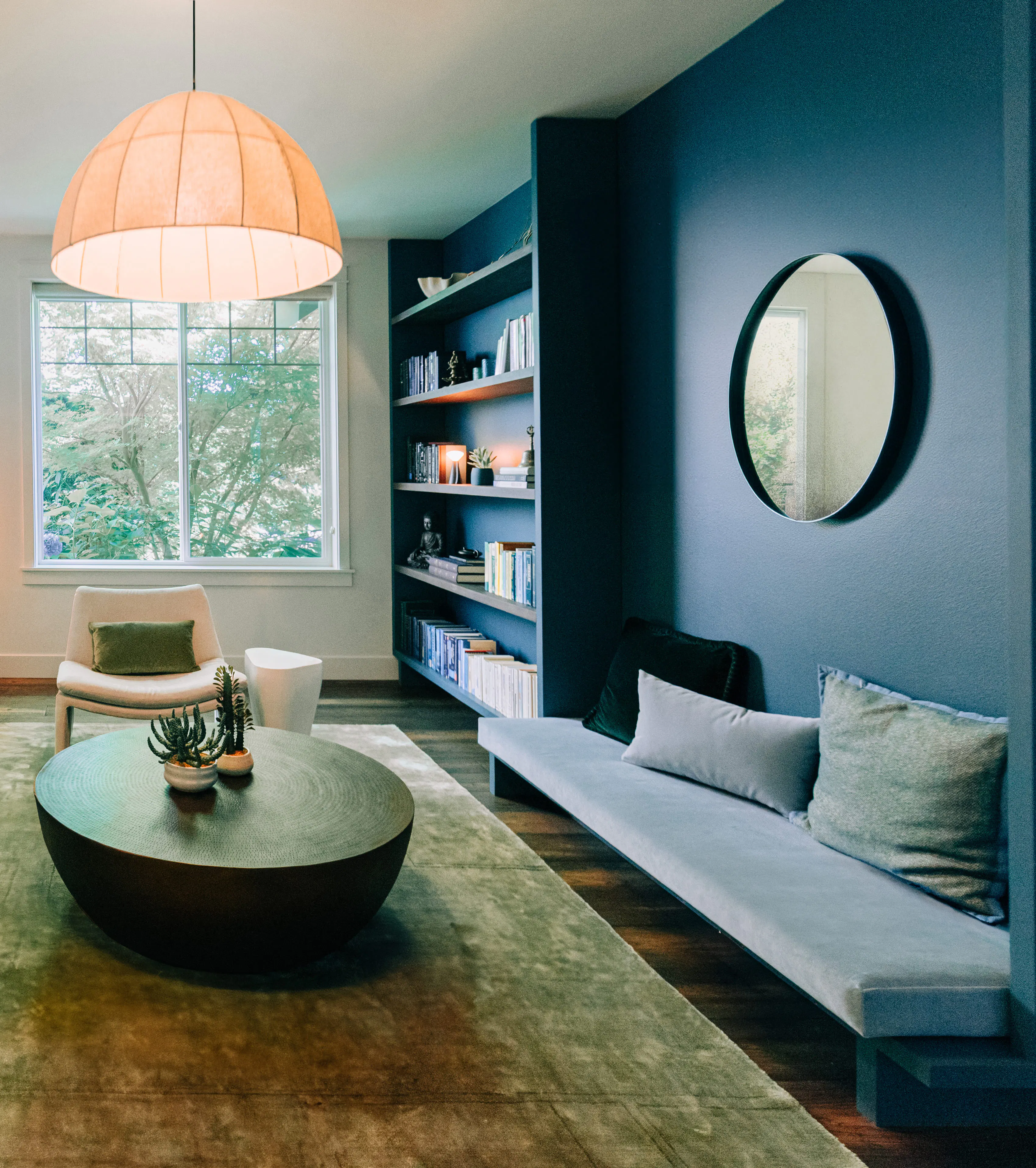 Designed by Persimmon Design, this home library pairs deep moody blue and greens, warm wood tones, and soft modern furnishings to create a space that feels both calming and sophisticated. Photo credit: Alexis Grosclaude
