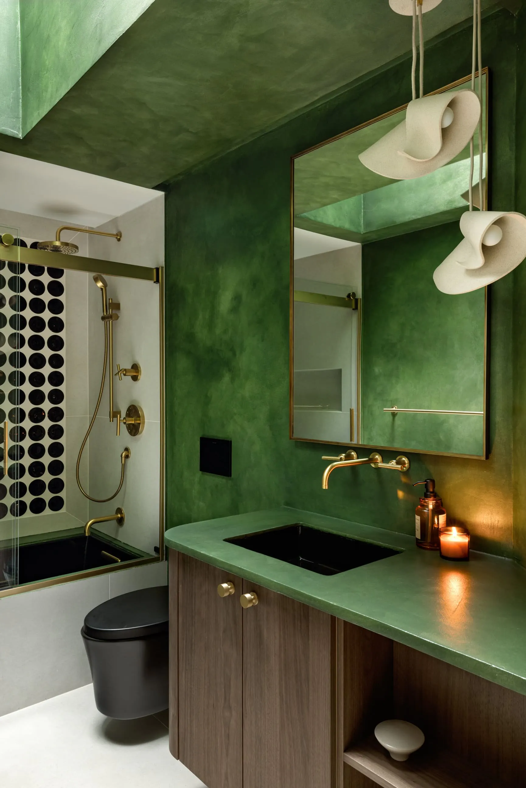 This bathroom by Persimmon Design is a perfect example of how thoughtful design can tailor a space to the family’s lifestyle, balancing the parents’ desire for a restorative sanctuary with the practical needs of young children.  By color drenching the space in highly durable green microcement, introducing sculptural lighting, designing a custom curved floating vanity, and transforming the shower wall into graphic art with playful round tiles, the remodel created an immersive retreat.