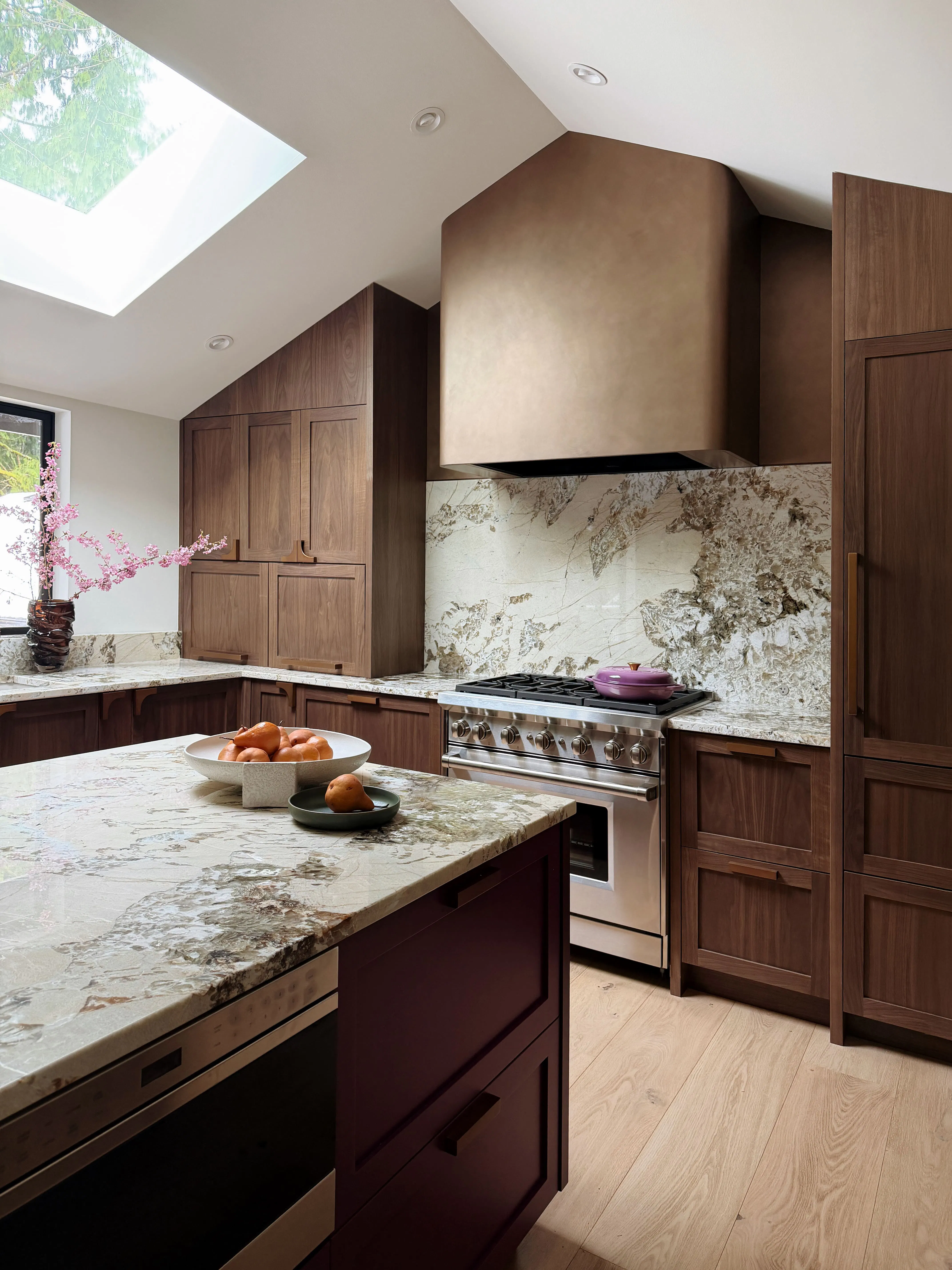 This kitchen rendering by Persimmon Design is a perfect example of why hiring a designer early can completely reshape what is possible within a home. The design reimagines the architecture by transforming it to a light-filled gathering space. White Oak cabinetry wraps the room, while softly illuminated niches, sculptural curves, and layered lighting create a feeling that is both grounded and quietly luxurious. The oversized island becomes more than a workspace — it becomes the heart of the home, designed for slow mornings, shared meals, and the rhythms of everyday life.