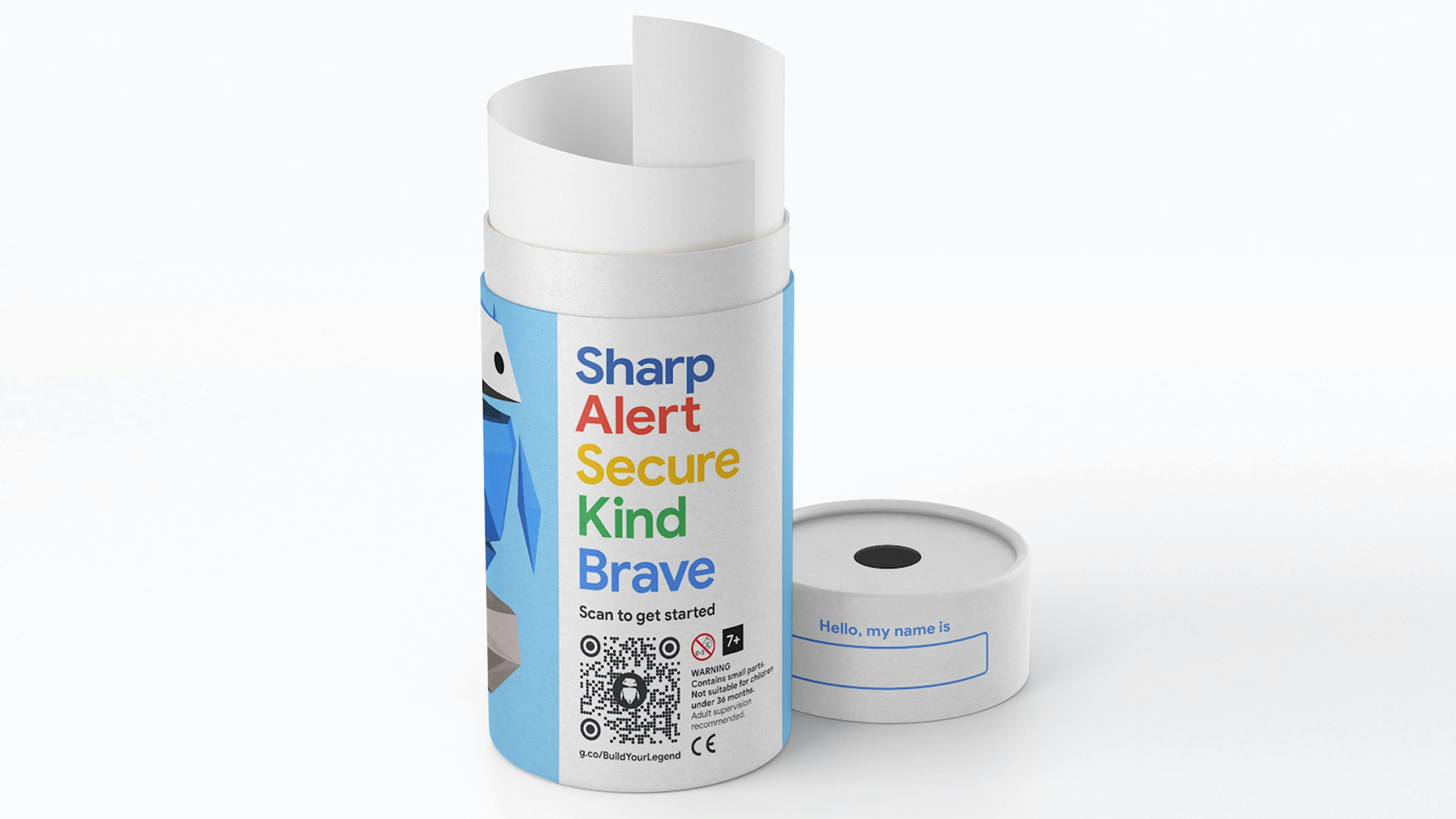 The product packaging for a 'Build Your Legend' activity kit. It consists of a white cardboard tube containing rolled-up materials. The tube's label features a blue geometric character, colorful text 'Sharp, Alert, Secure, Kind, Brave,' a QR code, and a URL. The lid is placed next to it and has a 'Hello, my name is' label.
