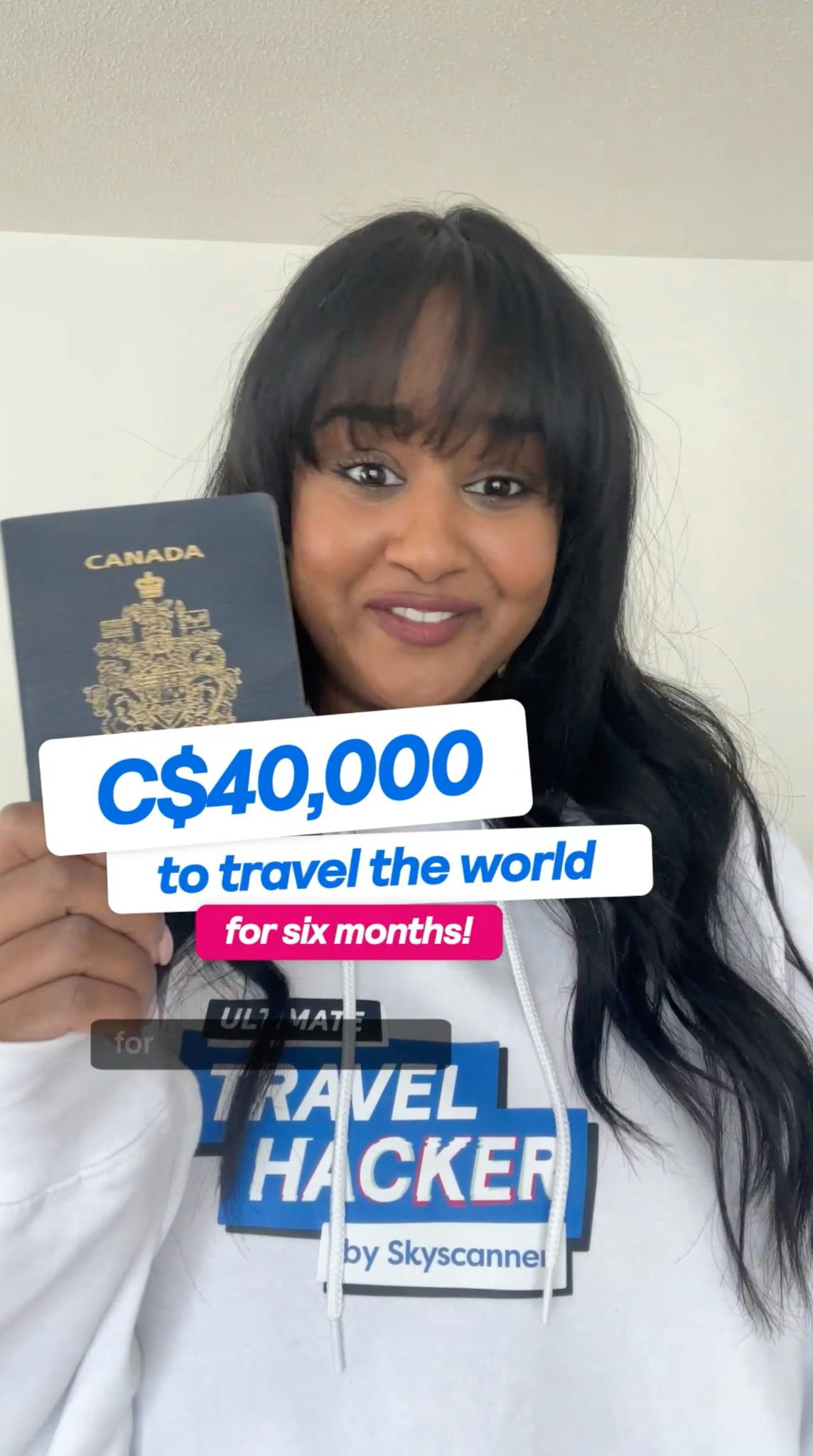A woman with long dark hair and bangs, wearing a white hooded sweatshirt with drawstrings and the 'ULTIMATE TRAVEL HACKER by Skyscanner' logo, smiles pleasantly at the camera. She is holding up a dark blue Canadian passport, which features the gold Canadian coat of arms. Layered text overlays are prominent: 'C$40,000' in blue text on a white banner, 'to travel the world' in white text on a blue banner below it, and 'for six months!' in white text on a bright pink banner at the bottom of the stack. A partially visible black subtitle banner at the very bottom of the frame shows the word 'for'. The background appears to be a plain, light-colored indoor wall.