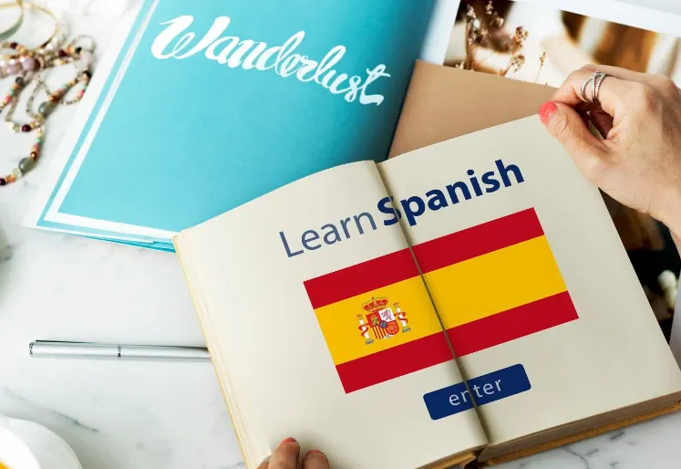 Pessoa segurando um livro aberto de aprendizado com bandeira da Espanha, com as palavras Learn Spanish e outro cartão de idiomas na imagem.