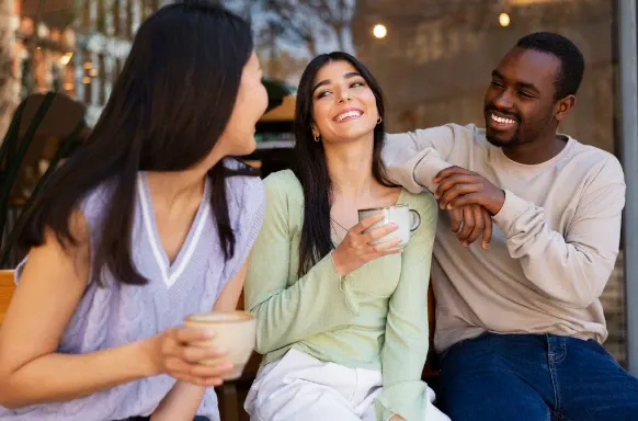 Amigos brindando com bebidas em um encontro ao ar livre, sorrindo e conversando ao entardecer, com iluminação aconchegante ao fundo.
