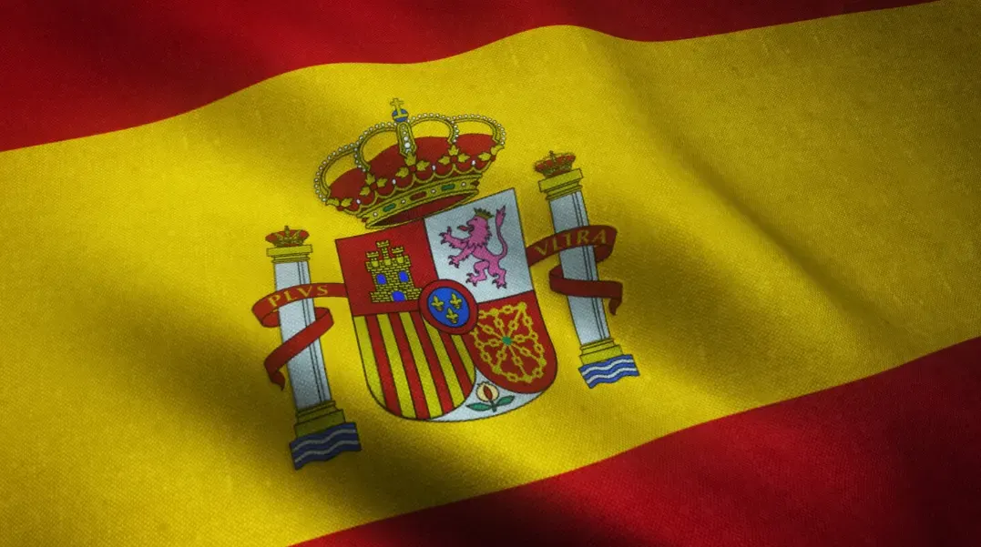Bandeira da Espanha ao fundo, com o brasão de armas central e listras vermelhas e amarelas visíveis no tecido ondulante.