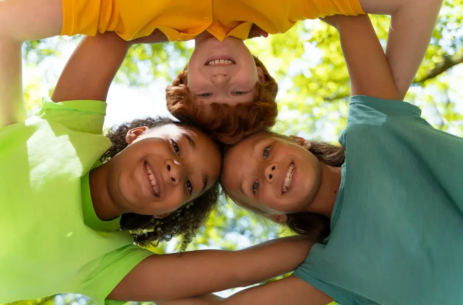 Quatro pessoas sorrindo em estilo selfie, em ambiente externo, com fundo desfocado de árvores e verde, transmitindo alegria e união entre amigos ou família.