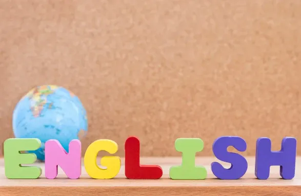 Palavra ENGLISH em letras coloridas sobre uma superfície bege, com um globo terrestre ao fundo, sugerindo aprendizado e idioma inglês.