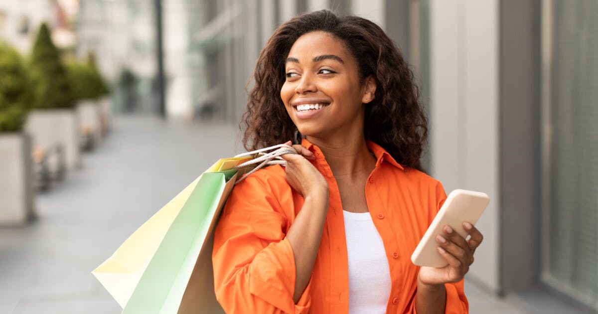 Uma mulher segurando sacolas de compras enquanto olha para o seu telefone.