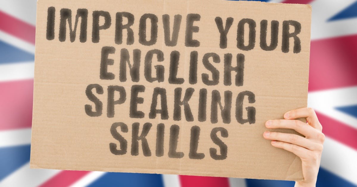 Uma mão segurando uma placa com a frase "Improve your English speaking skills", na frente de uma bandeira da Grã-Bretanha.