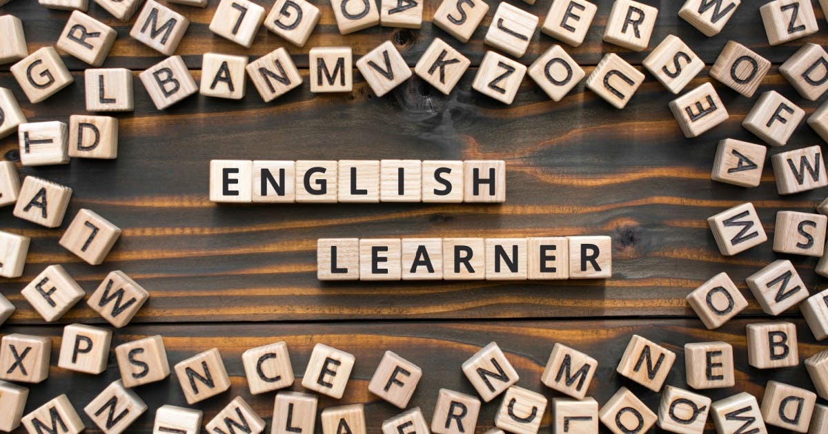Vários cubos com letras, espalhados e no centro da imagem alguns deles enfileirados, formando a frase "English Learner".
